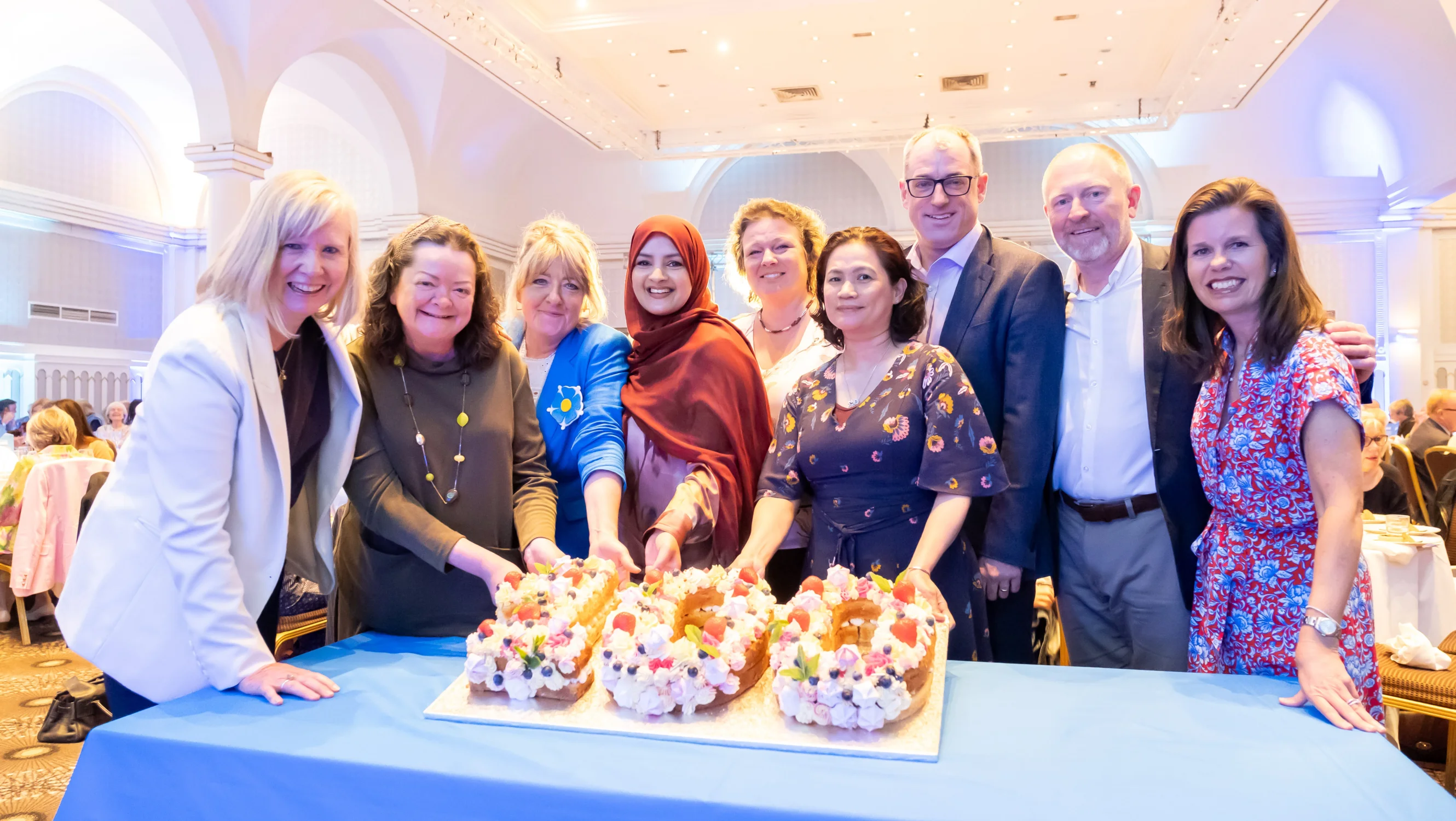 A group of people standing around and cutting a cake shaped like '100'.