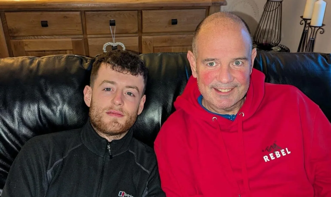 Lewis and his dad sat on a sofa smiling at the camera.