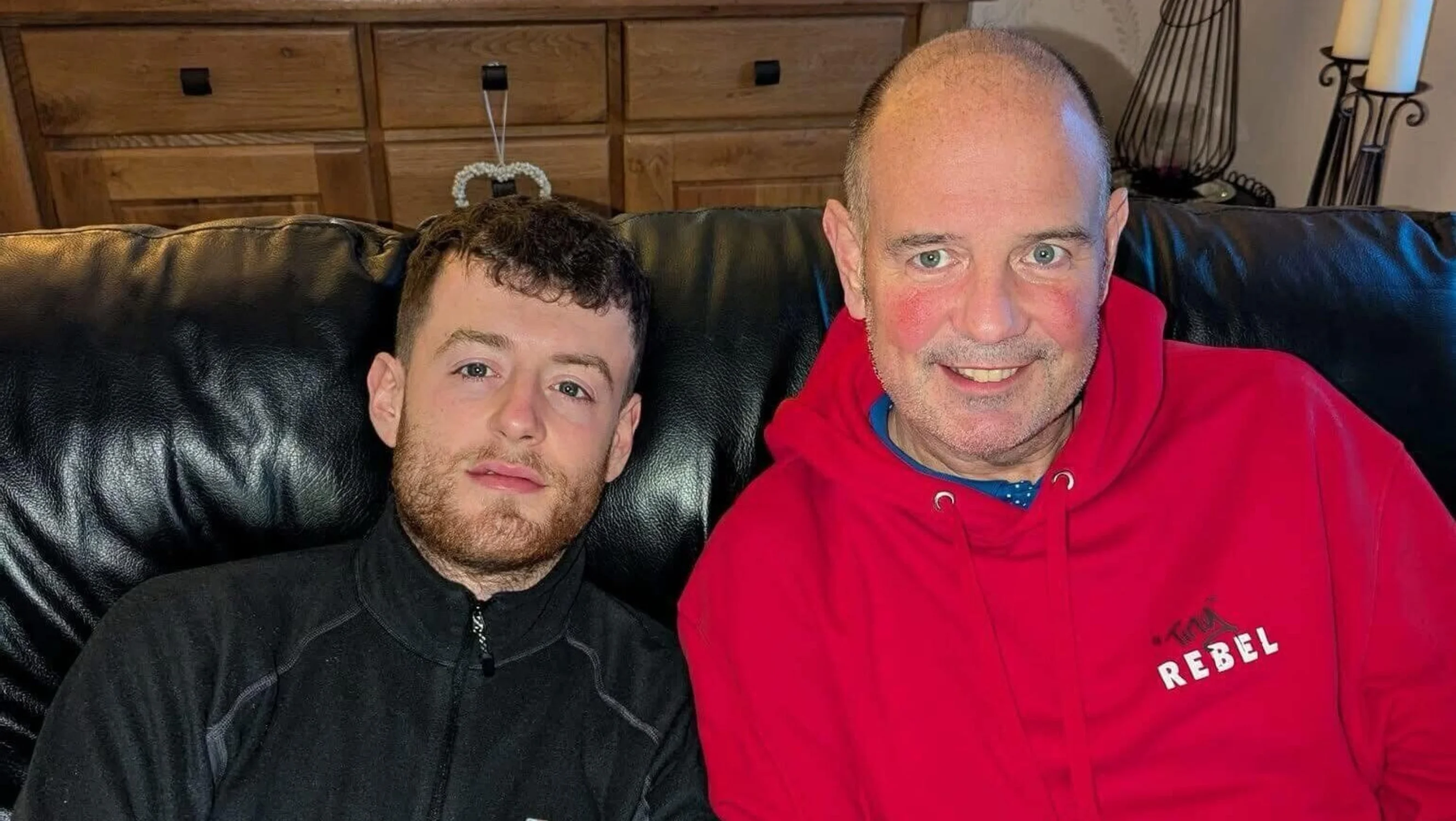 Lewis and his dad sat on a sofa smiling at the camera.