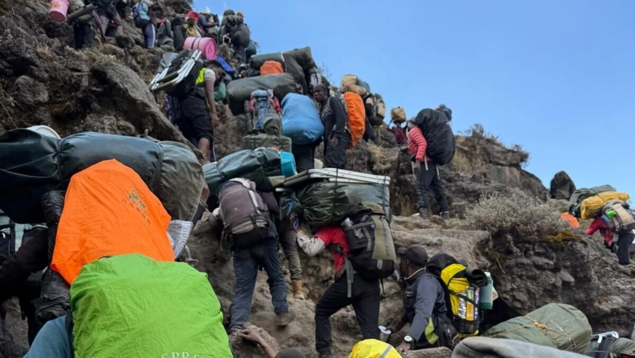 Lots of climbers wearing backpacks and hiking gear climbing the surface of the mountain.