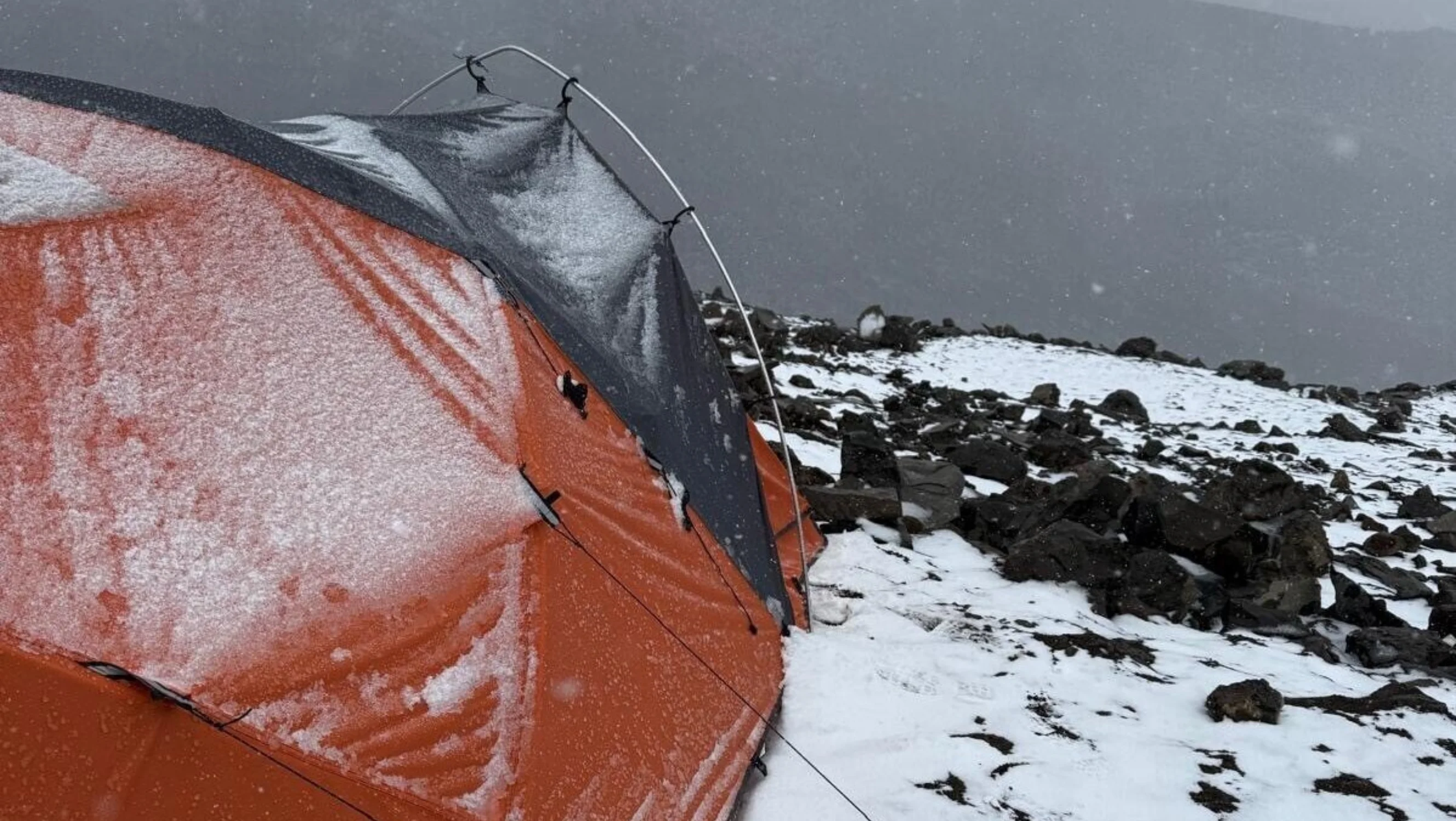 An orange tent in the snow overlooking the edge of a mountain.