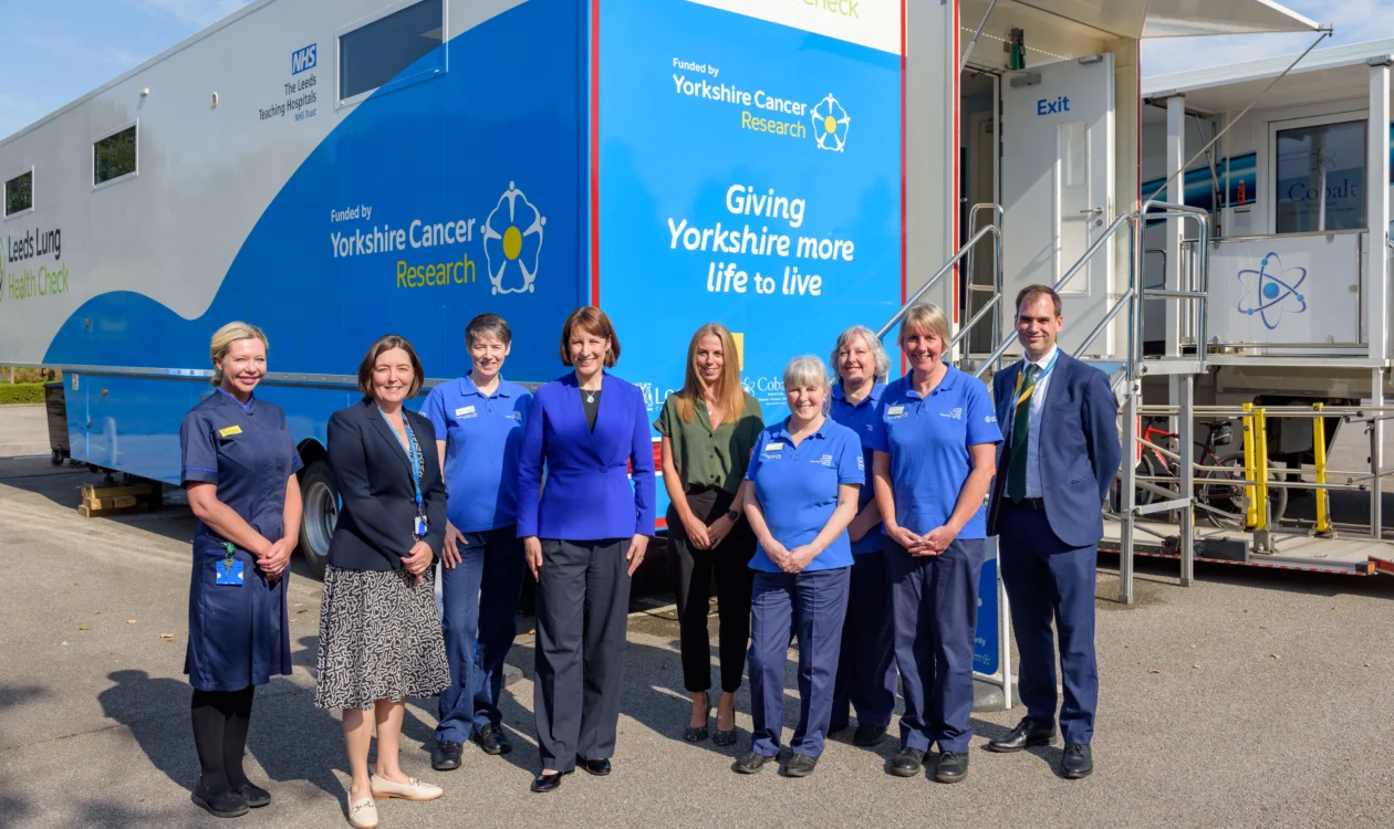 9 people stood outside of the Leeds Lung Health Check van smiling at the camera.