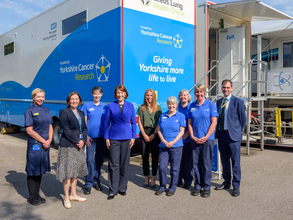 9 people stood outside of the Leeds Lung Health Check van smiling at the camera.