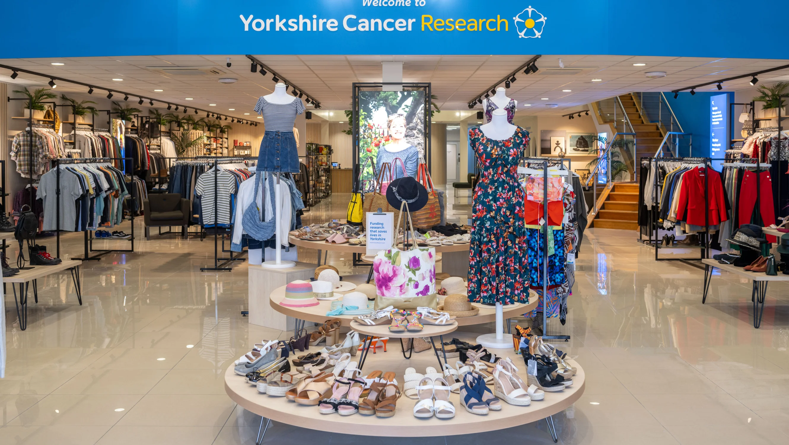 A display of spring/summer women's clothing at the entrance of the shop. There's mannequins wearing floral outfits and in the background there's an expanse of men's and women's clothing displays.