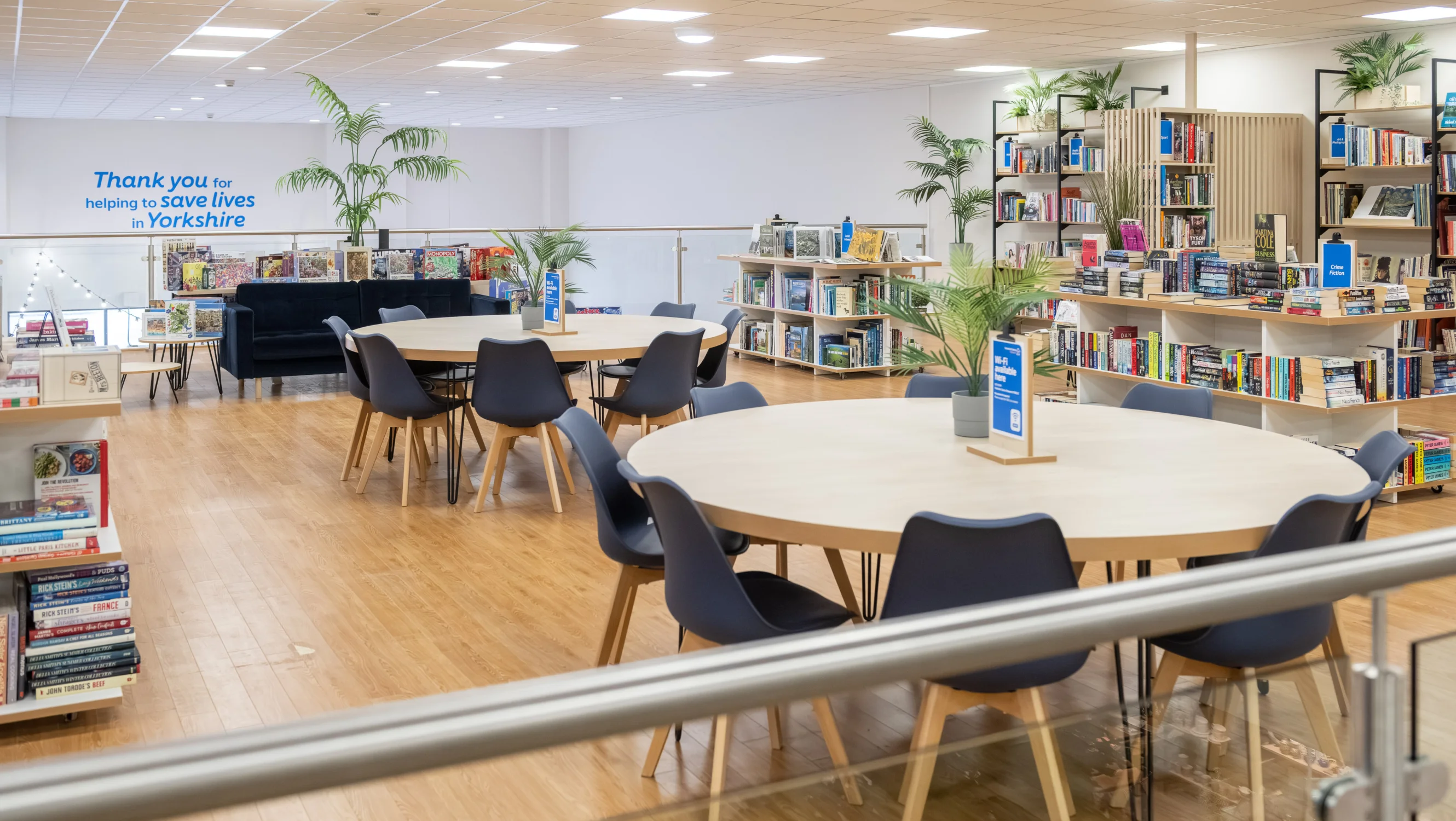 Two circular tables with eight chairs at each in a community space. Behind them, you can see book shop displays and fake plants.