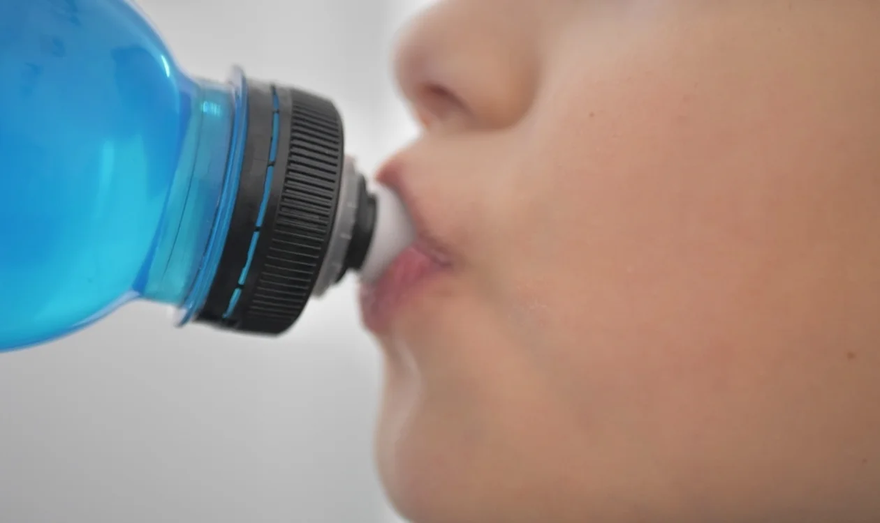 A child drinking a blue liquid from a plastic bottle