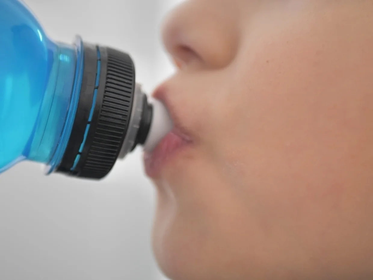 A child drinking a blue liquid from a plastic bottle