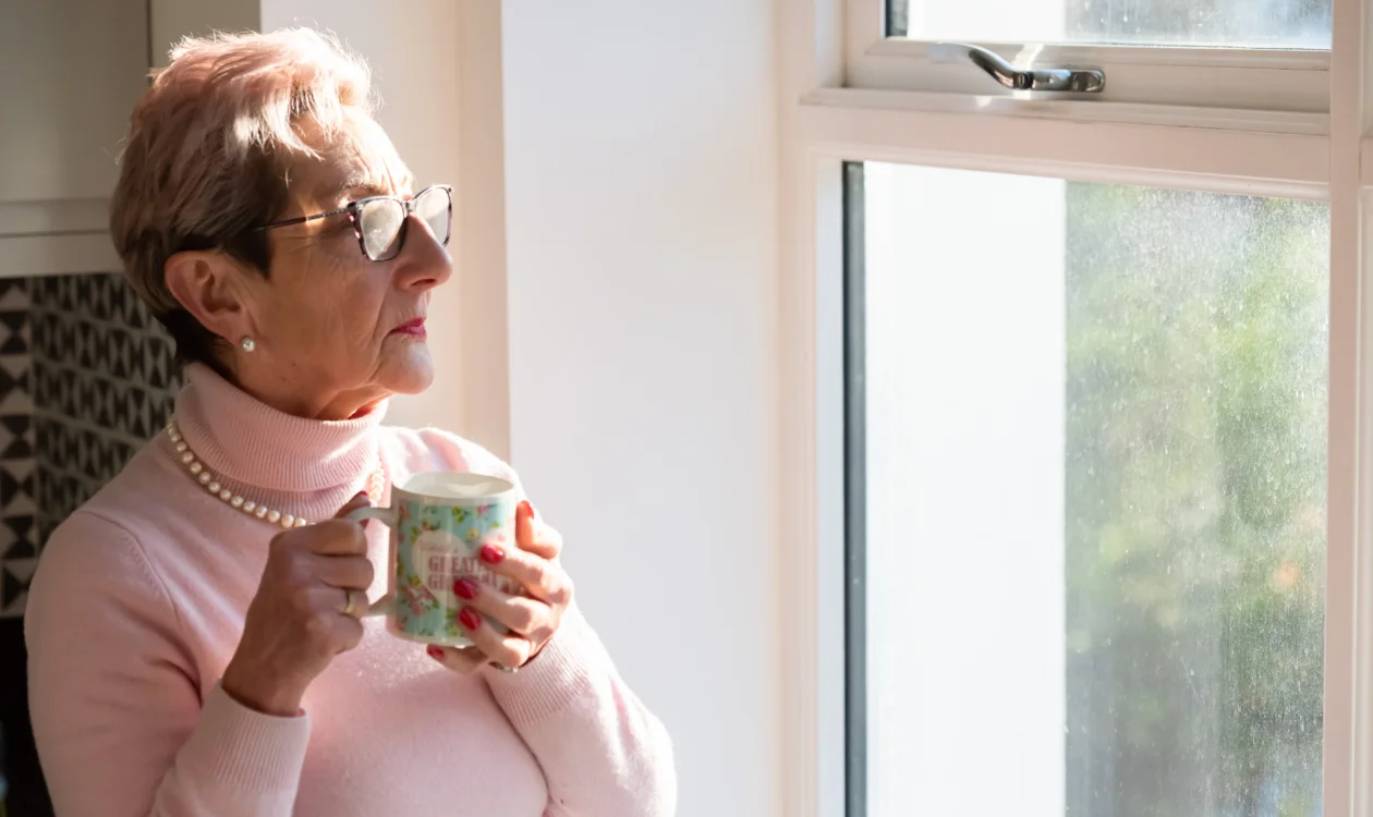 Diane looking out of a window and holding a mug