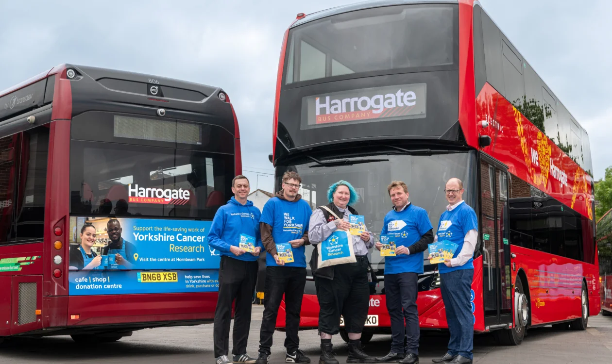 Five people stand in front of the Yorkshire Cancer Research branded bus. The four men are wearing a blue Yorkshire Cancer Research tops and Sarah, in the middle, is carrying a tote bag from the charity.