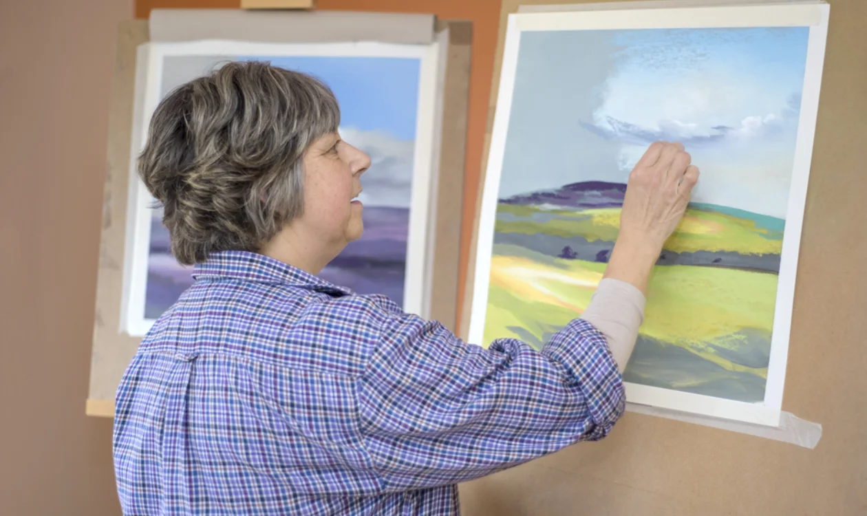 Lucia Smith drawing with oil pastels. She is creating a countryside landscape.