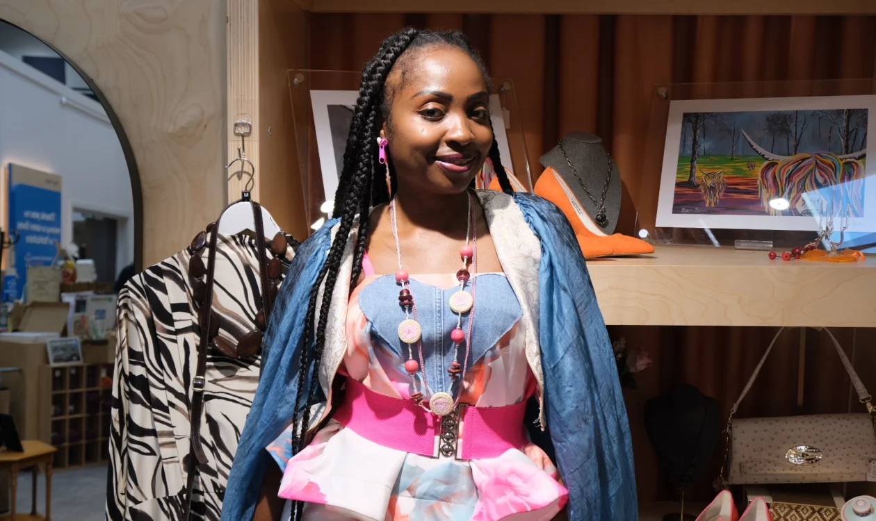 Goodness is standing in front of some shop shelves smiling at the camera