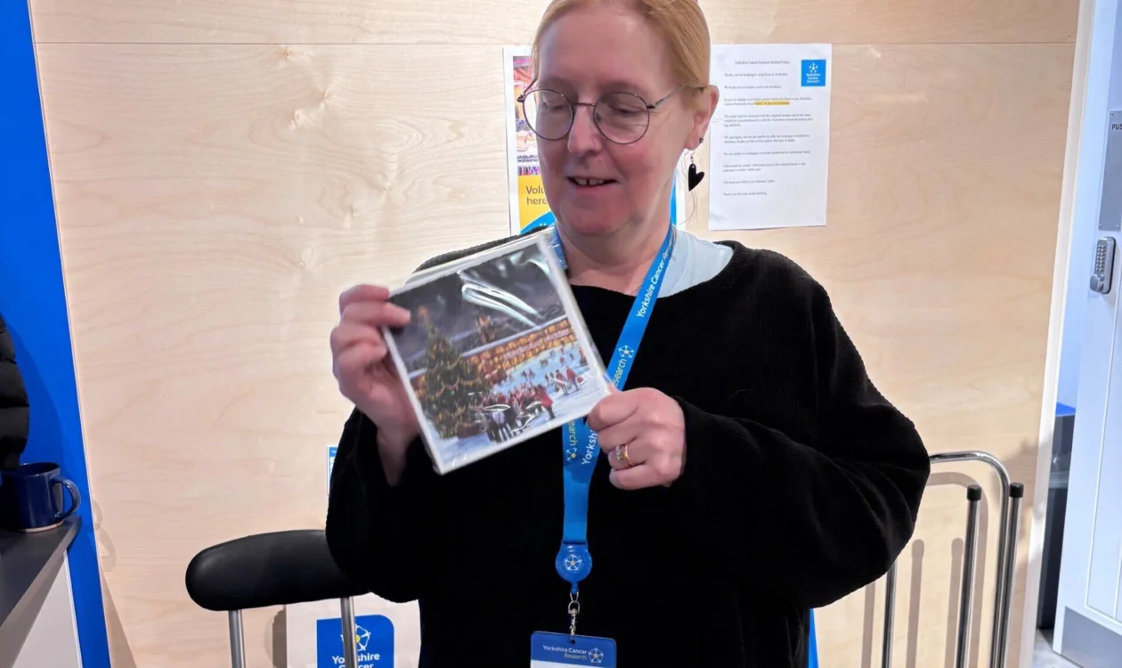 Chris is holding a Christmas card with an illustration of Halifax in the Yorkshire Cancer Research shop in Halifax.