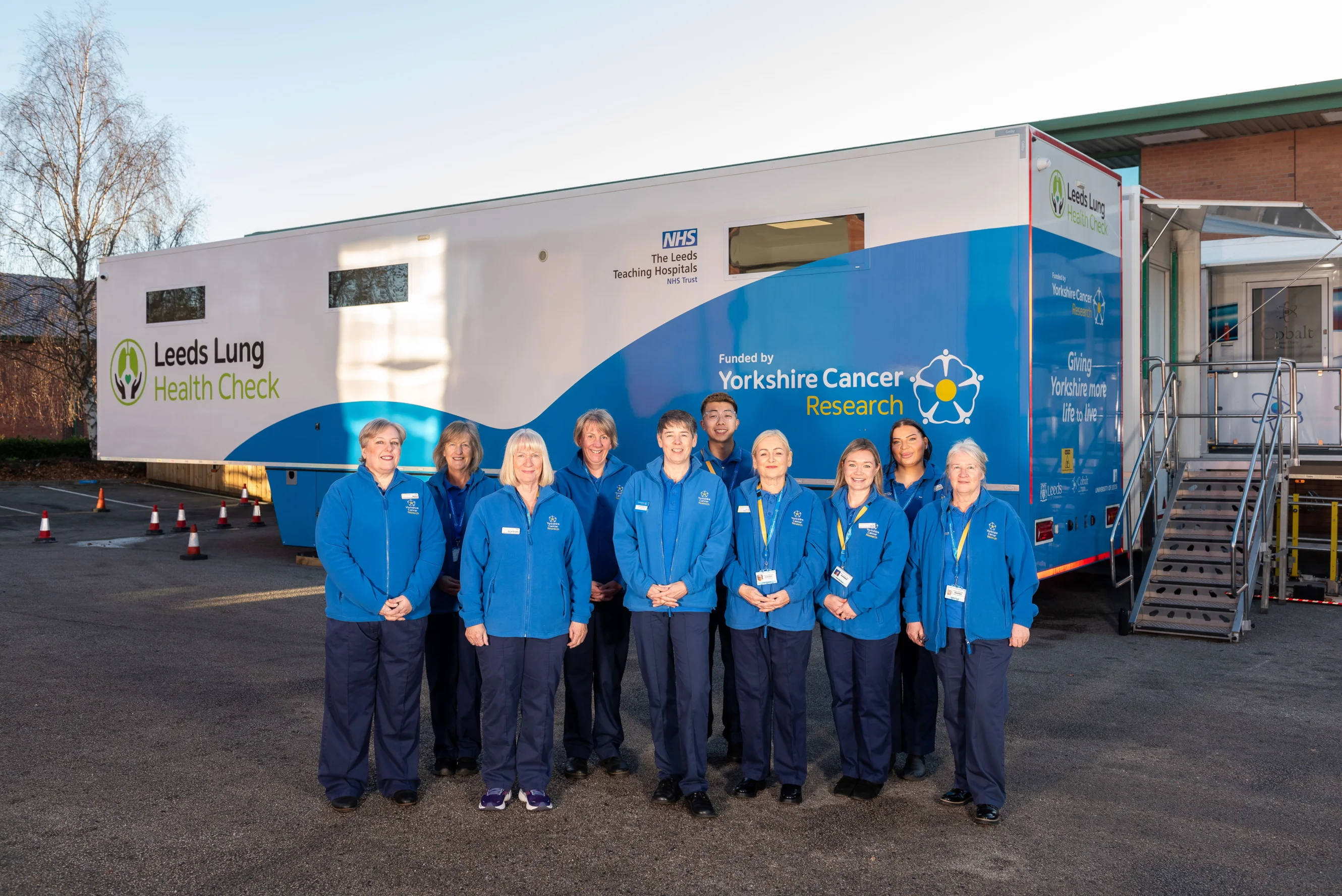 A large group of people standing in front of a blue and white Leeds Lung Health Check van