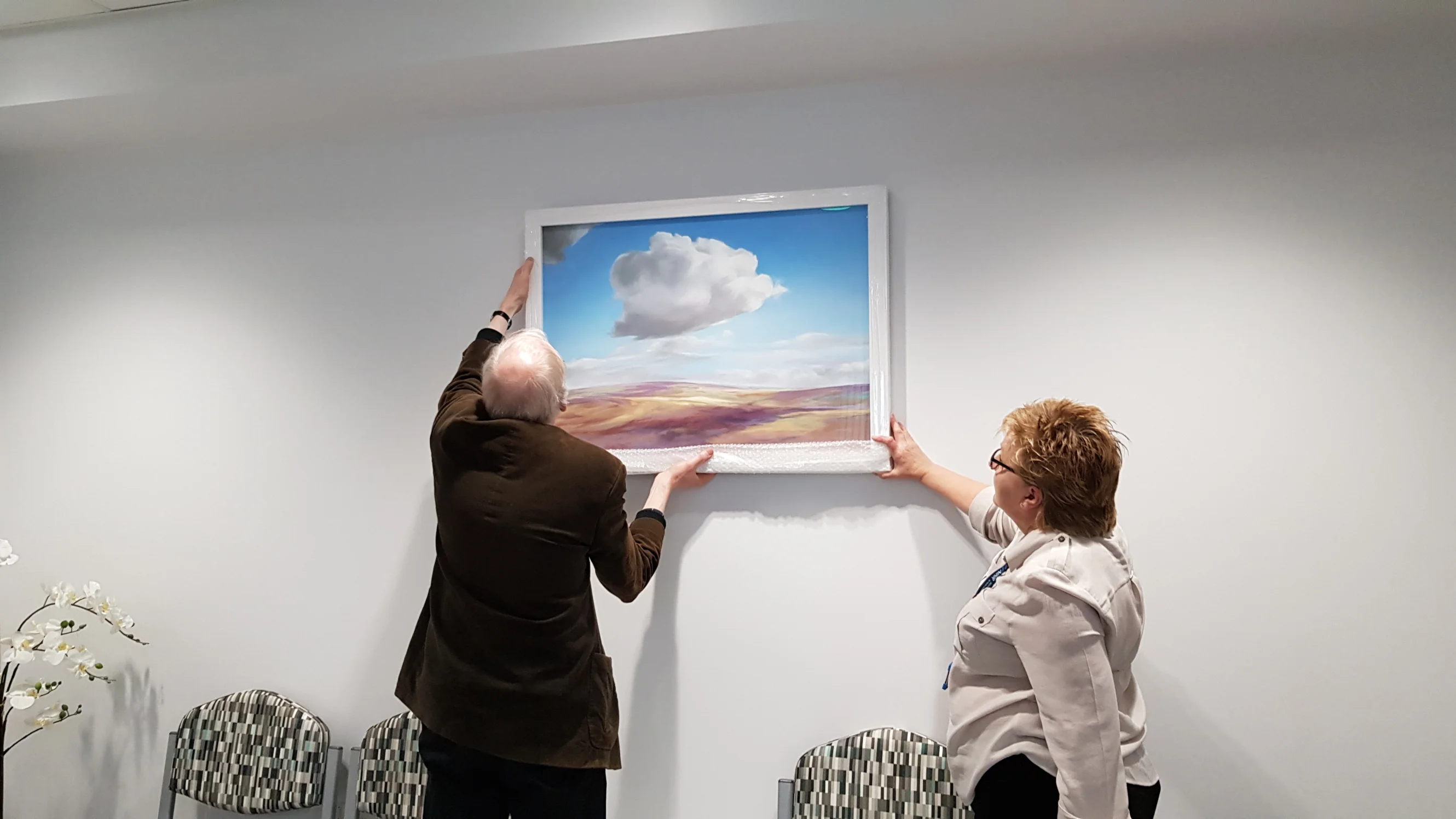Lucia's art being hung at the Bexley wing in Leeds. It is a countryside landscape featuring a large cloud.