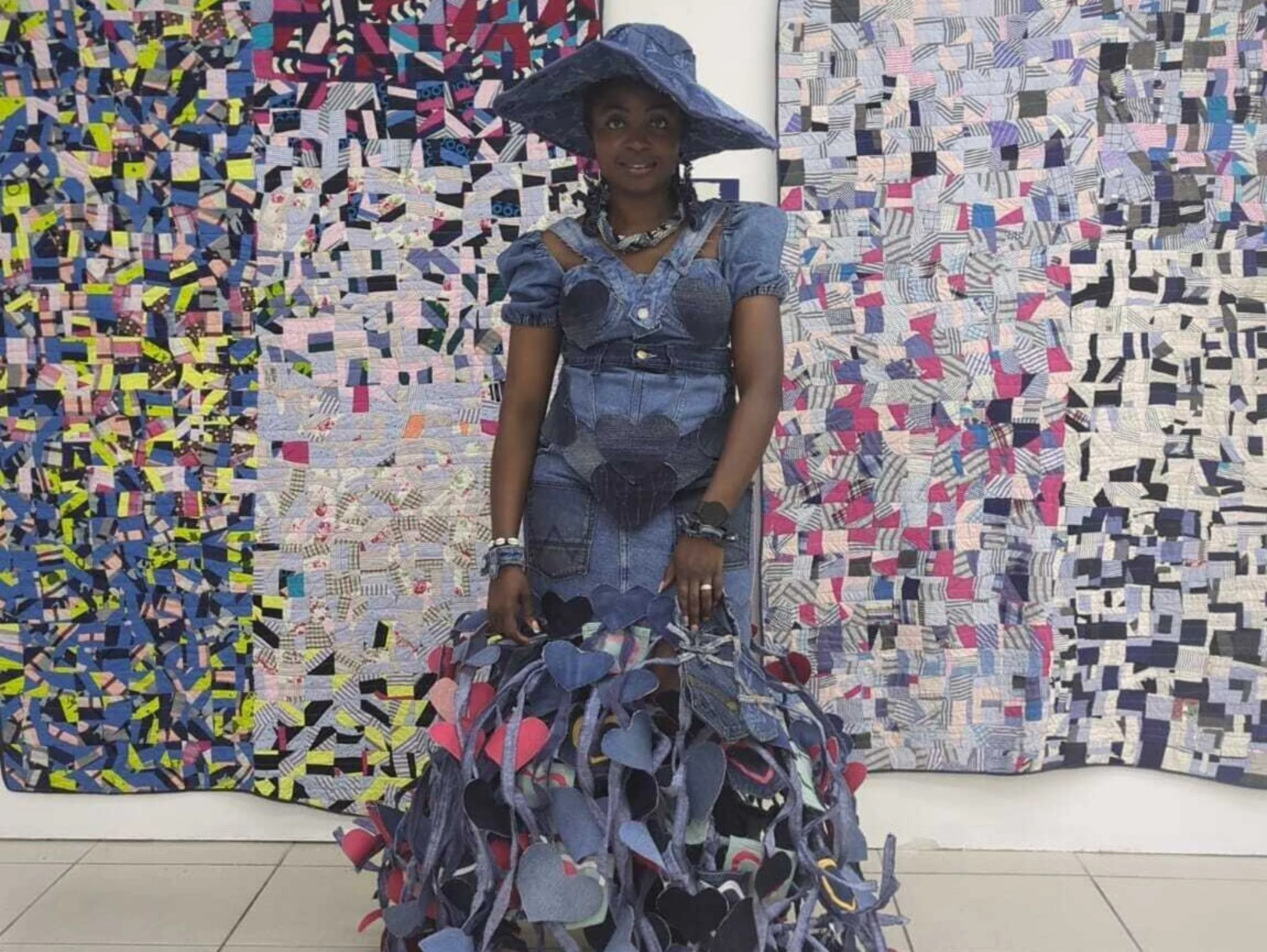 a lady wearing an extravagant gown made from upcycled denim is standing in front of two large contemporary piece if artwork.