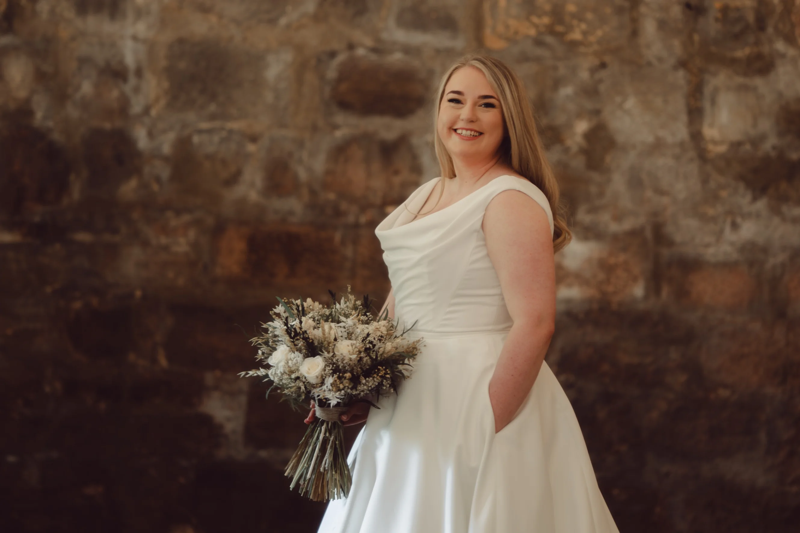 Aimee is stood in her wedding dress holding a bouquet of flowers