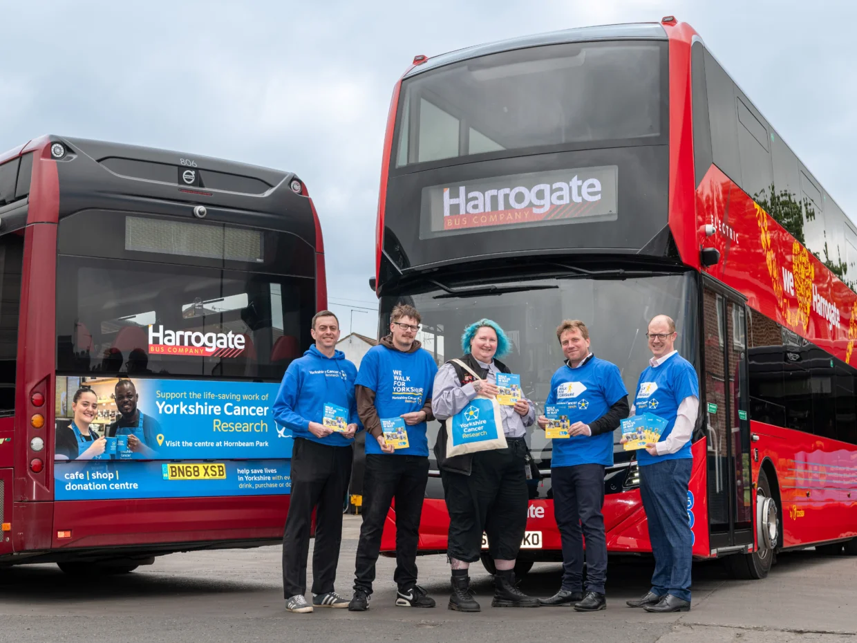 Five people stand in front of the Yorkshire Cancer Research branded bus. The four men are wearing a blue Yorkshire Cancer Research tops and Sarah, in the middle, is carrying a tote bag from the charity.