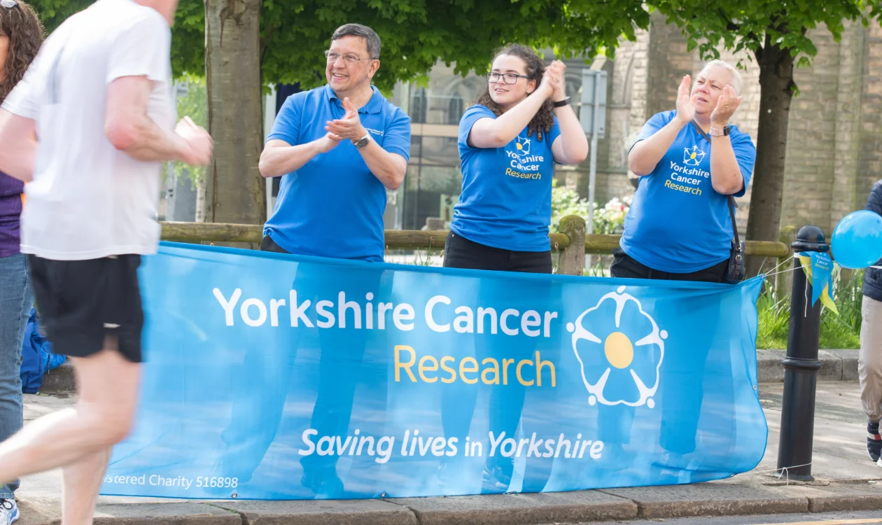 A group of people in front of a Yorkshire Cancer research banner clap passing runners.