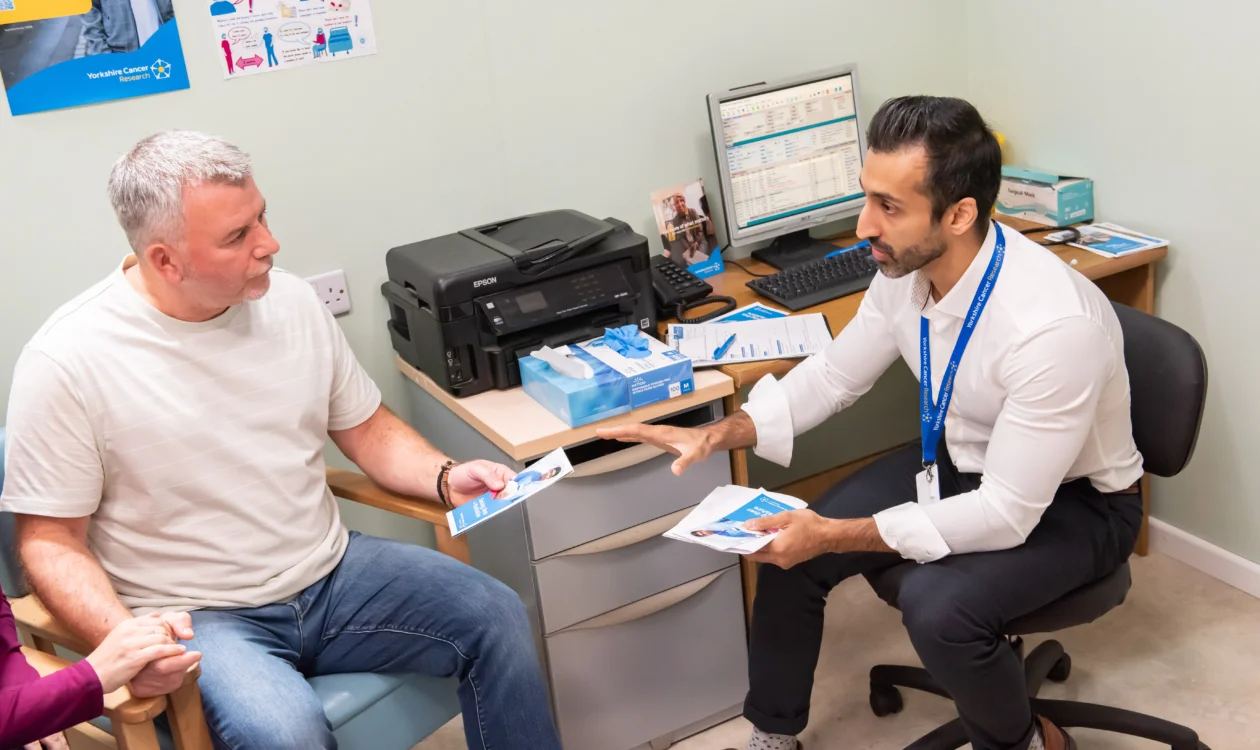 A doctor is handing a man a brochure in his office, they are both sat down.