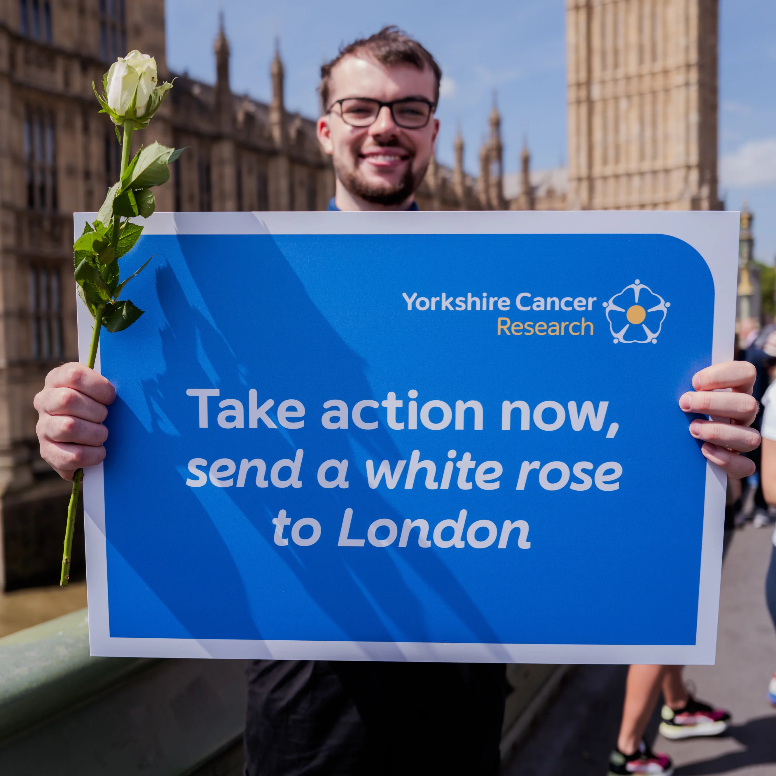Fred Giles holding a sign saying 'Take action now, send a white rose to London'