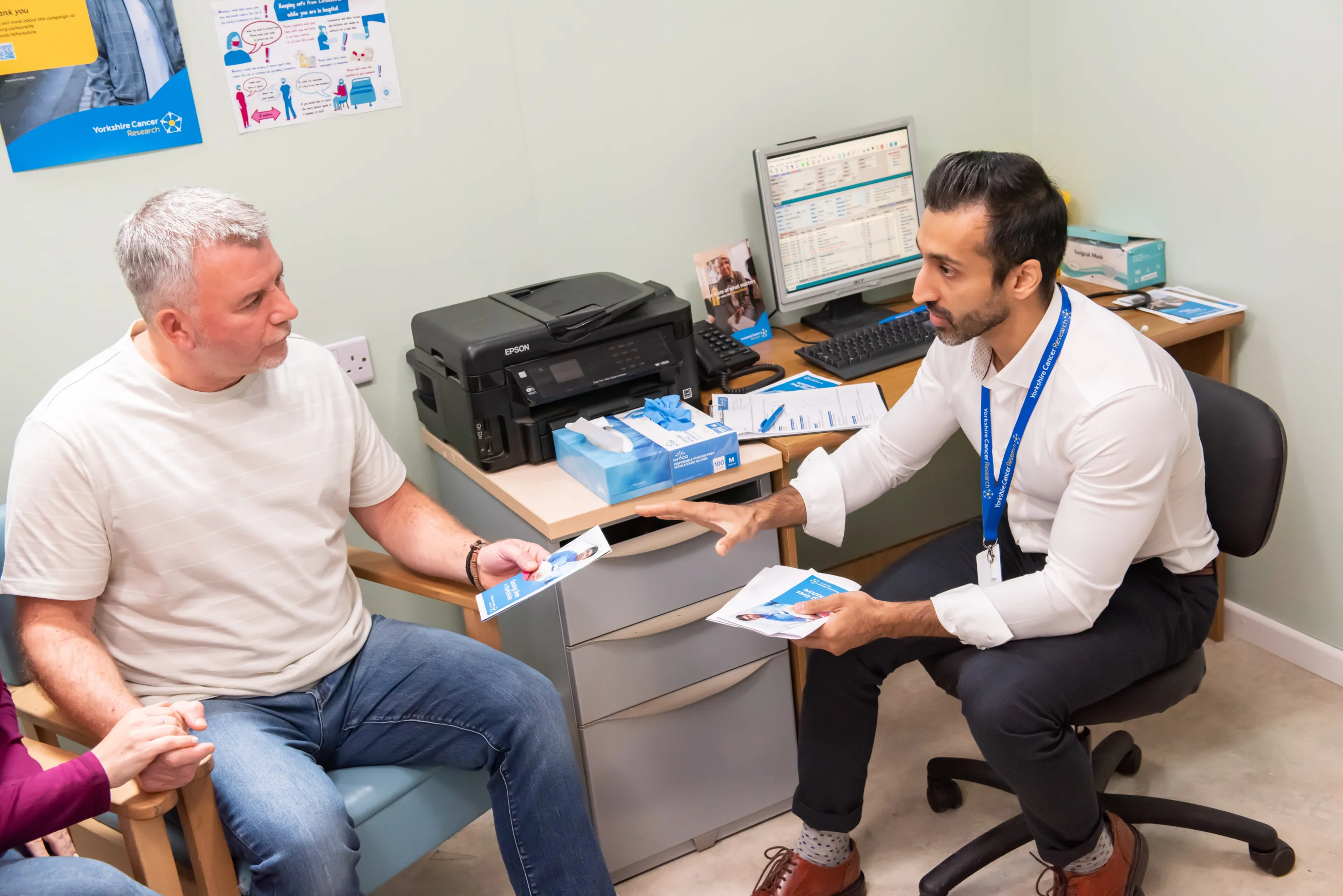 A doctor is handing a man a brochure in his office, they are both sat down.