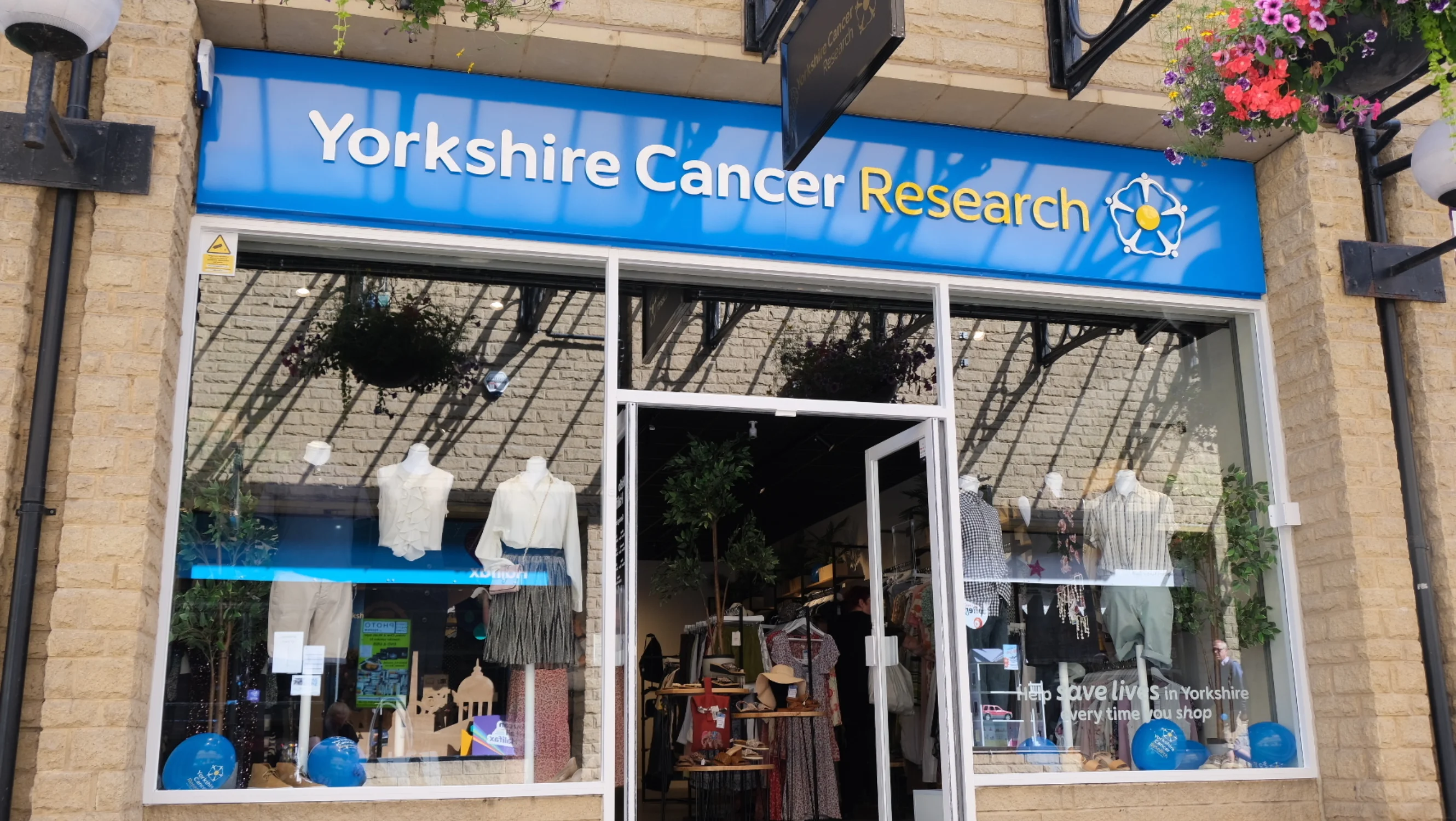 The exterior of the Halifax shop with two windows displaying mannequins and the charity's logo on a blue sign above the door.