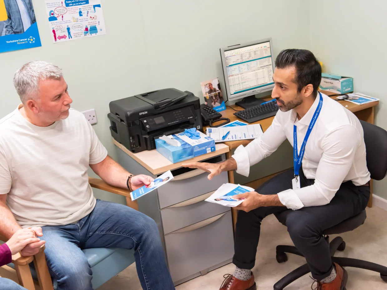 A doctor is handing a man a brochure in his office, they are both sat down.