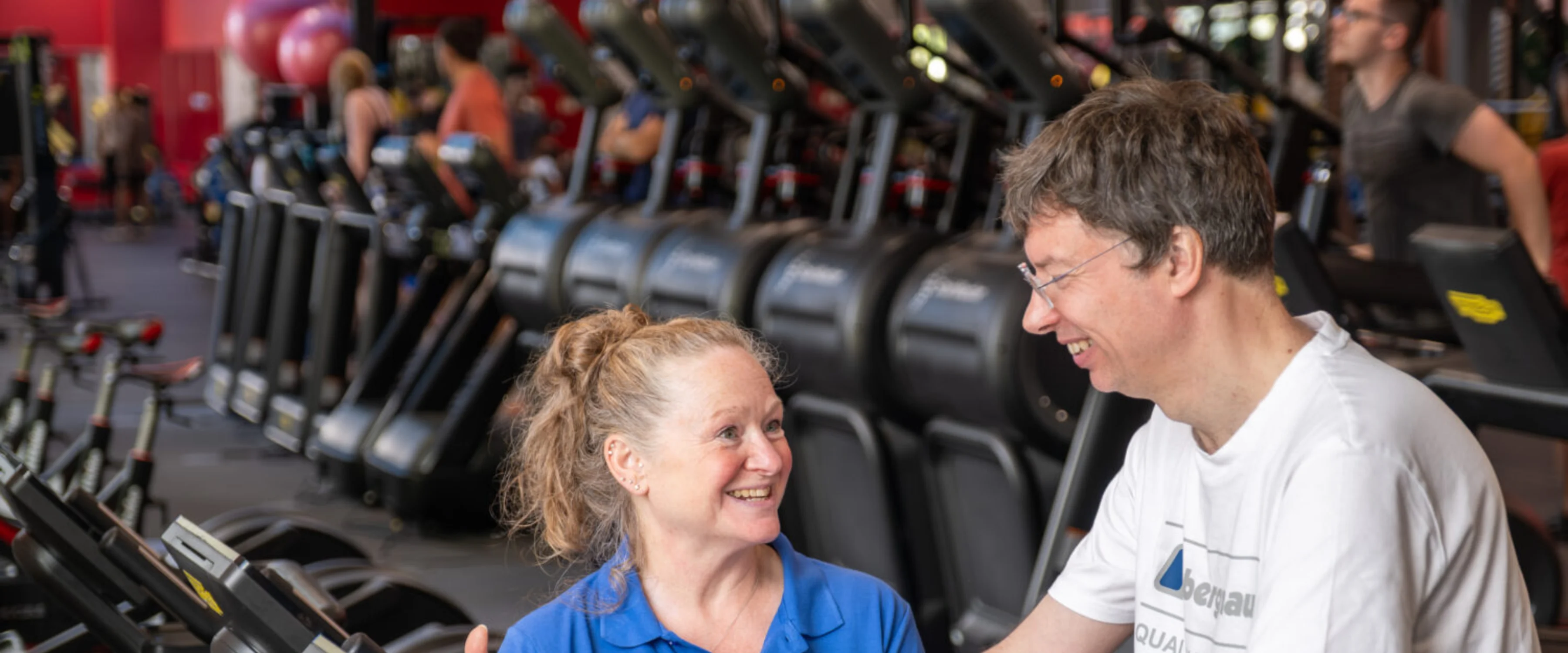 A man on a bike in a gym being supported by a member of staff
