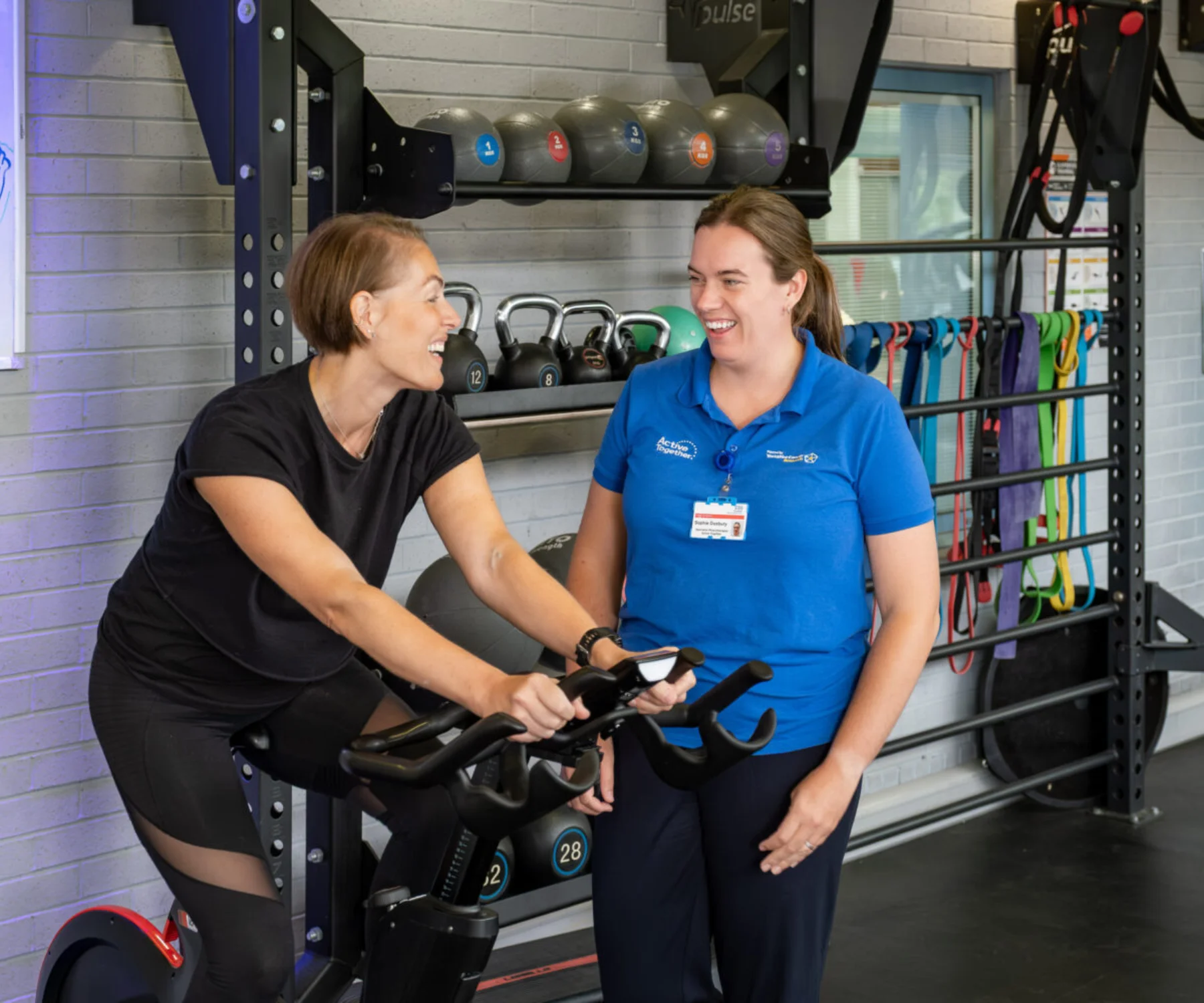 A person exercising on a bike in a gym with a member of staff dressed in blue
