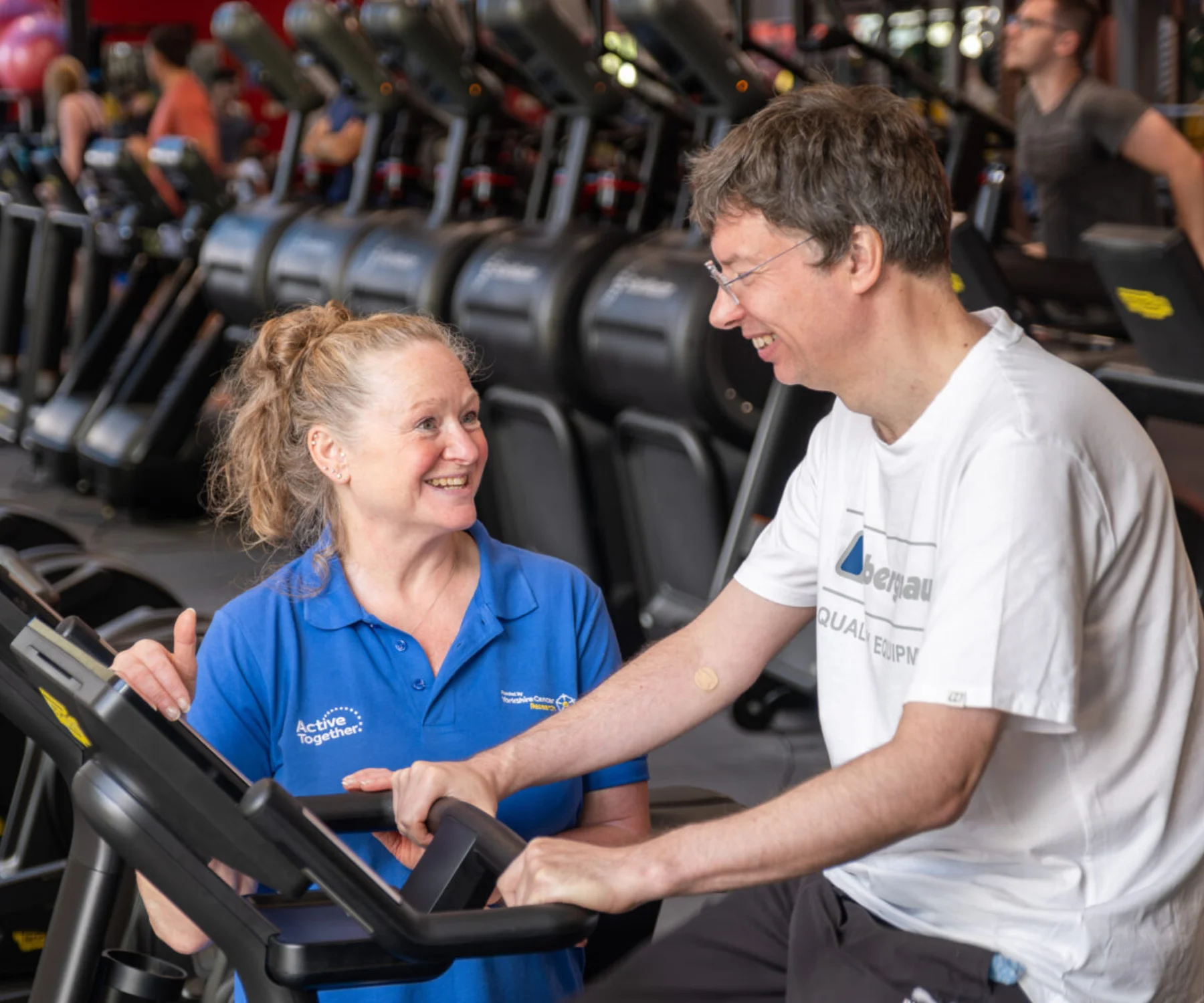 A man on a bike in a gym being supported by a member of staff