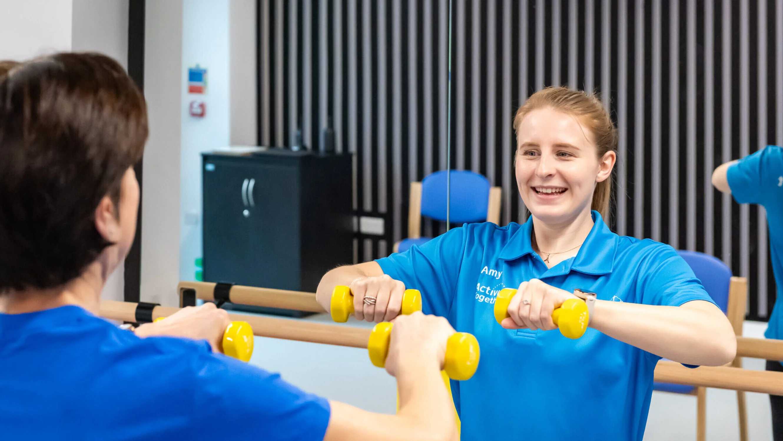 A woman exercising with weights in a gym with a fitness instructor