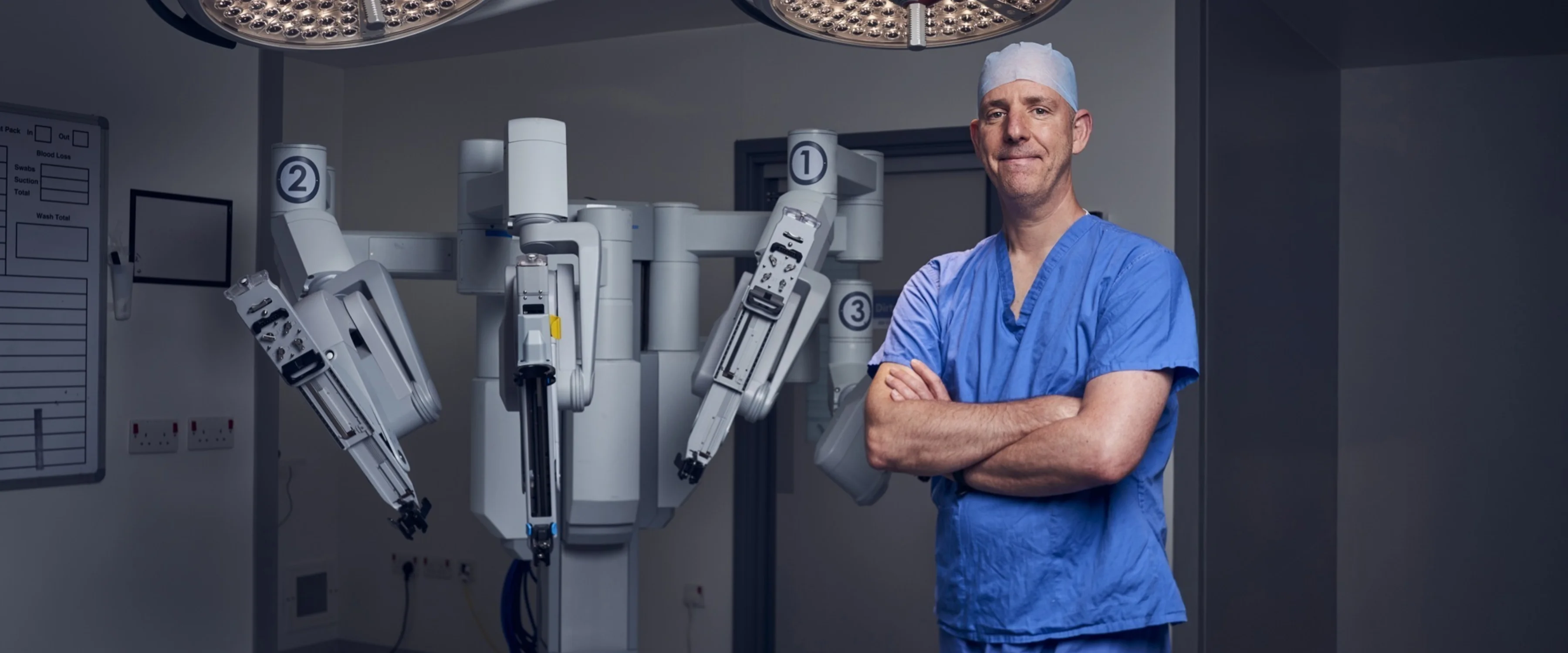 A medical professional wearing blue scrubs stands in front of large medical machinery