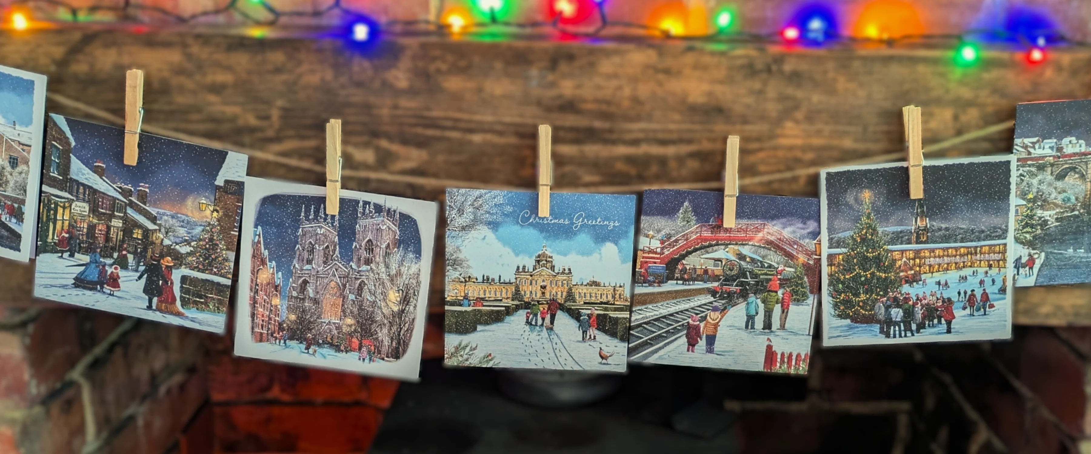 A selection of Christmassy Yorkshire scenes displayed in a string over a fireplace with Christmas lights