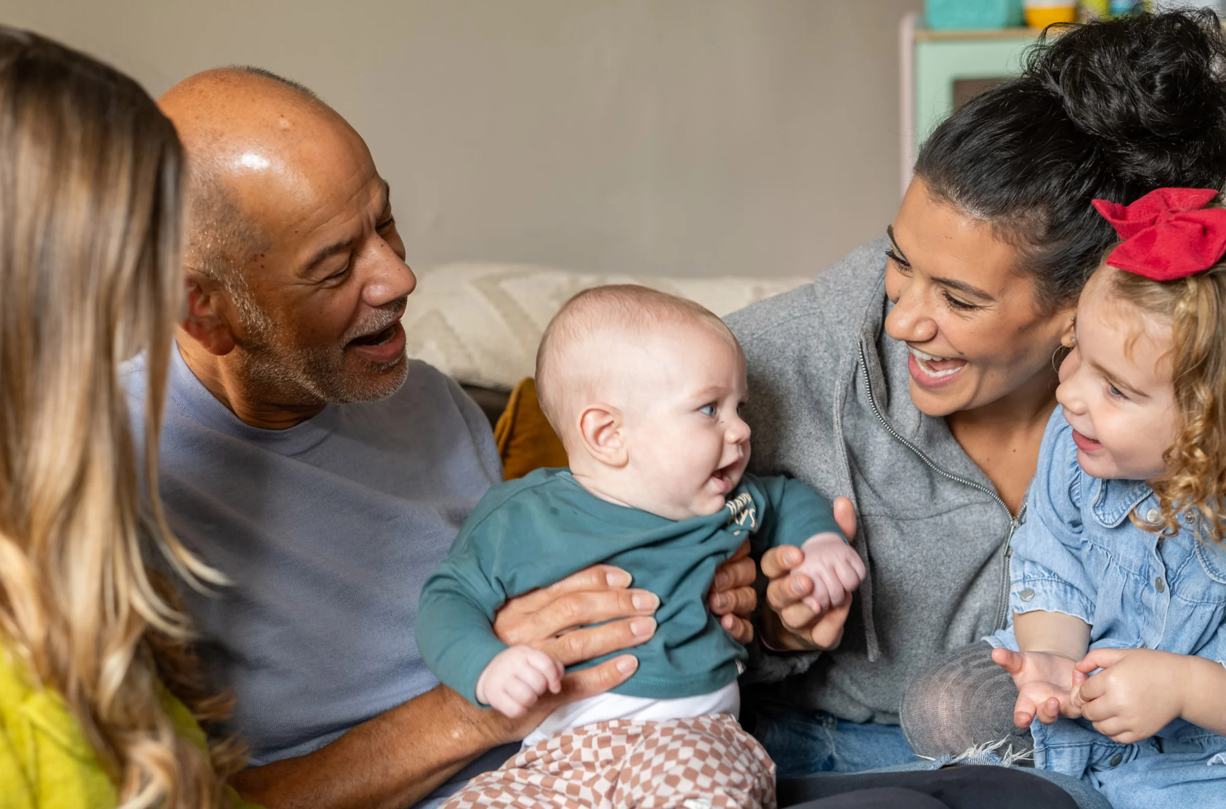 A family sit together on a sofa entertaining a baby