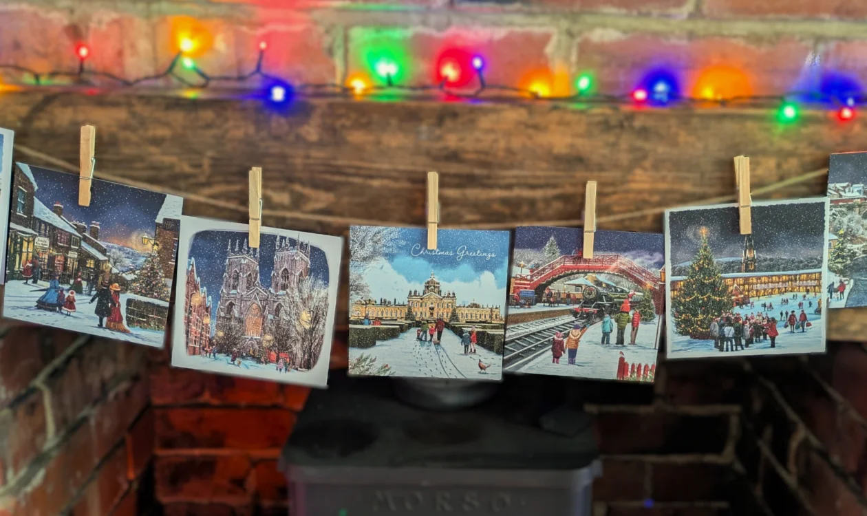 A selection of Christmassy Yorkshire scenes displayed in a string over a fireplace with Christmas lights