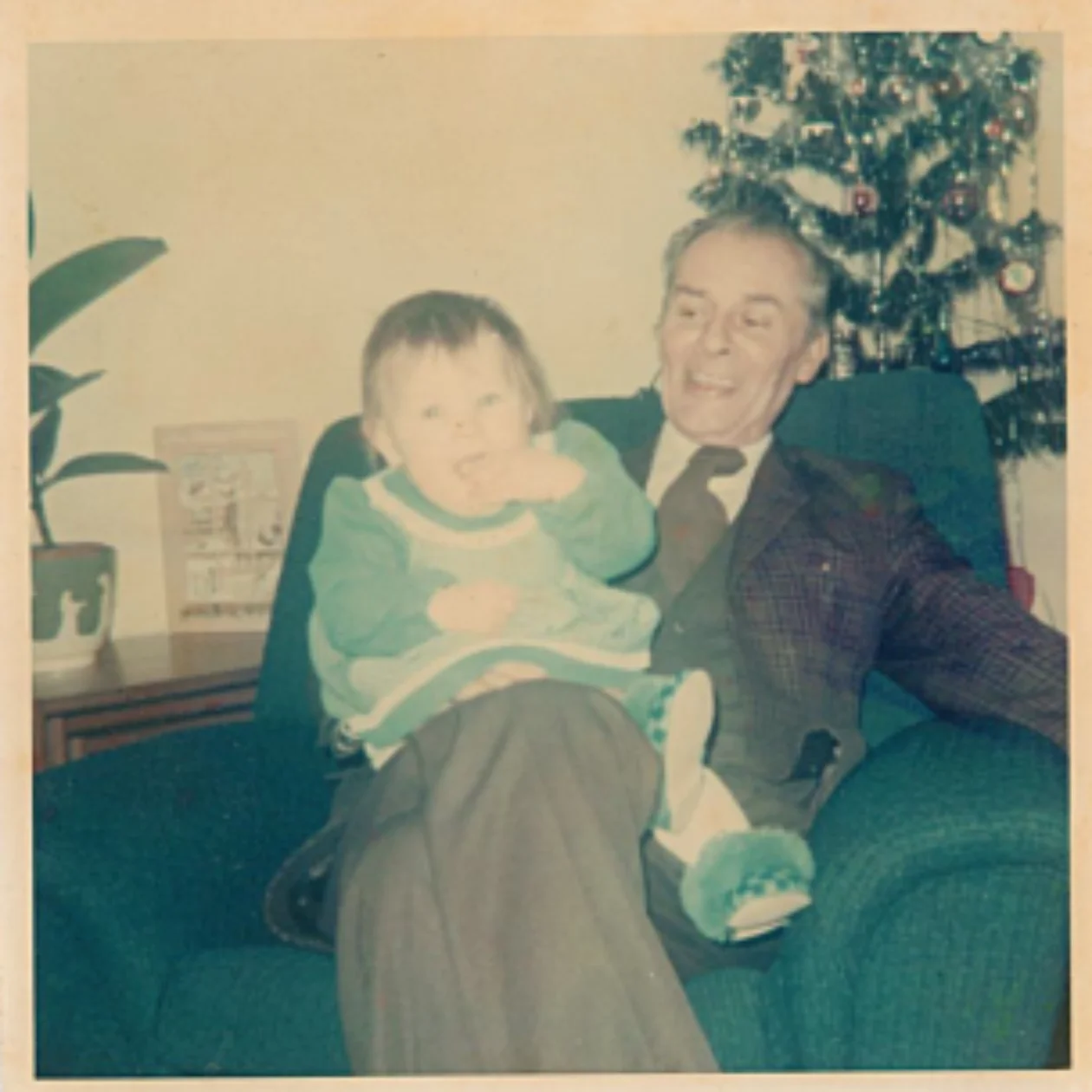 An old photograph of an older man with a small child on his knee, a Christmas tree in the background.