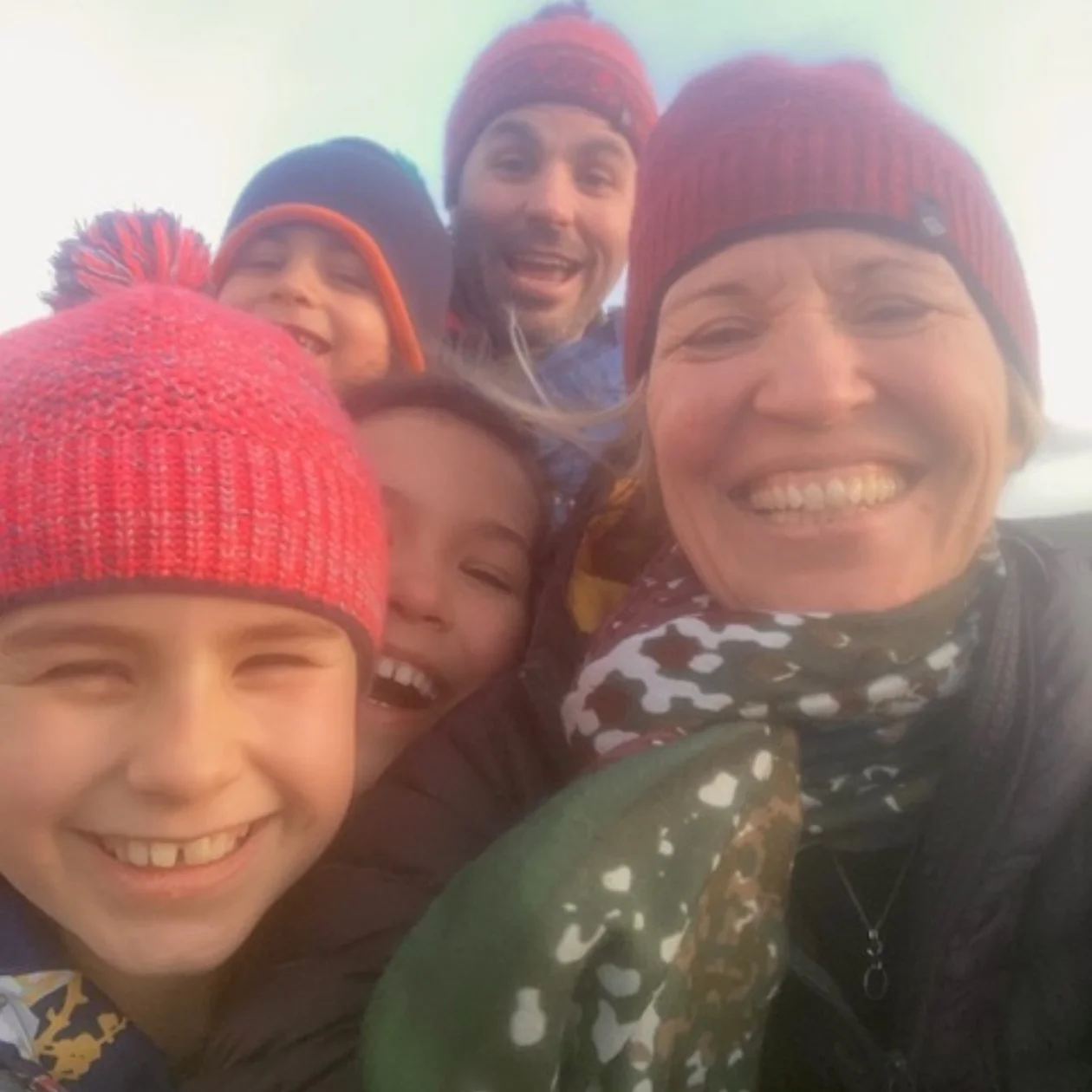 A family all wearing woolly hats gather close to take a smiling selfie