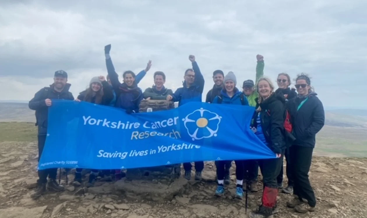 A group of people celebrating at the top of a hill holding a Yorkshire Cancer Research banner