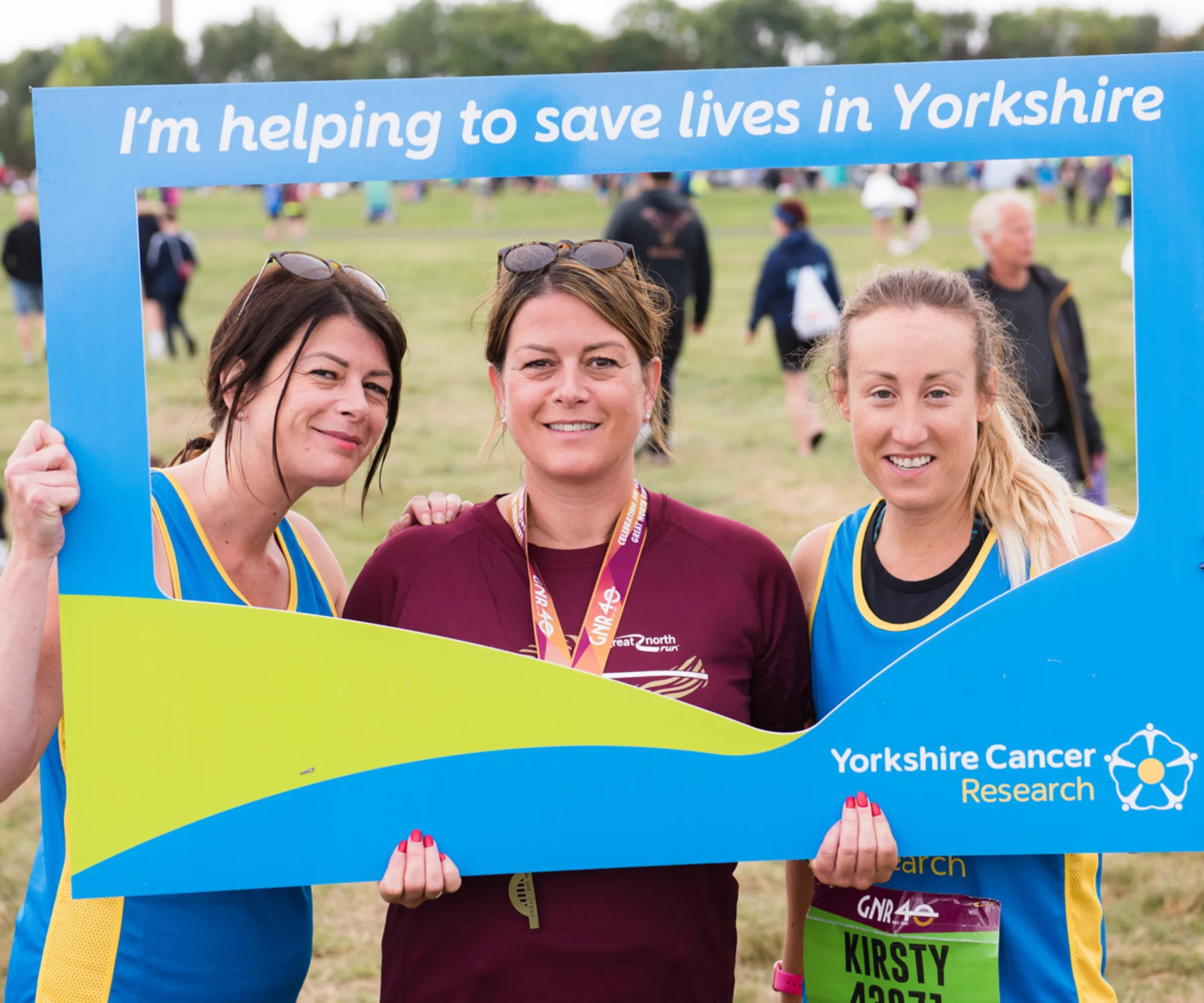 Three runners posing for a selfie after completing a race - using a 'selfie frame' which contains the phrase "I'm helping to save lives in Yorkshire"