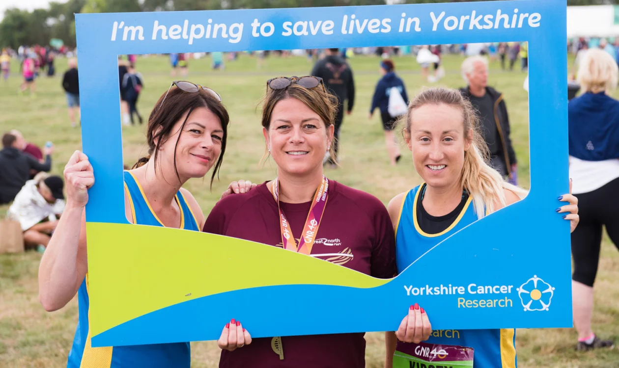 Three runners posing for a selfie after completing a race - using a 'selfie frame' which contains the phrase "I'm helping to save lives in Yorkshire"