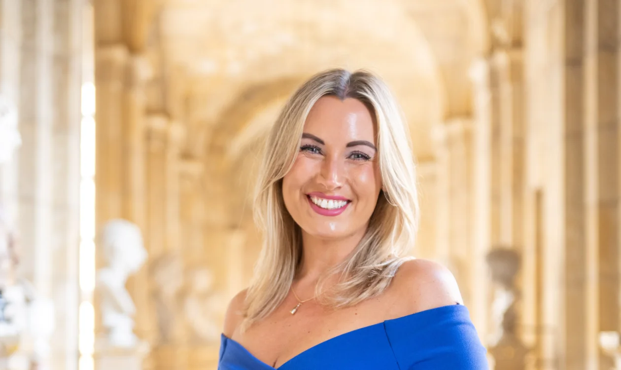 A lady in a blue formal dress stands in a grand corridor