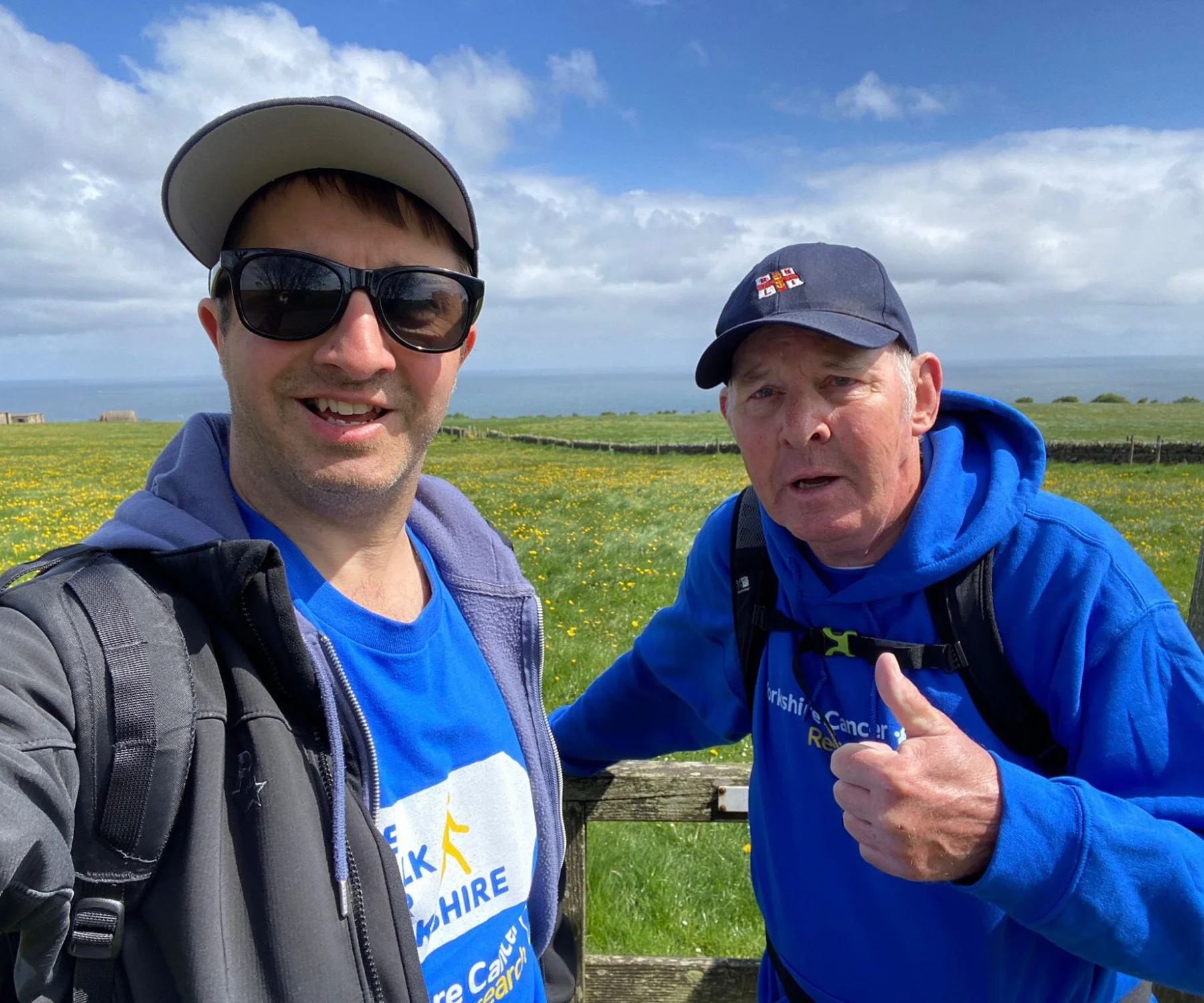 A younger and older man take a selfie on a coastal walk