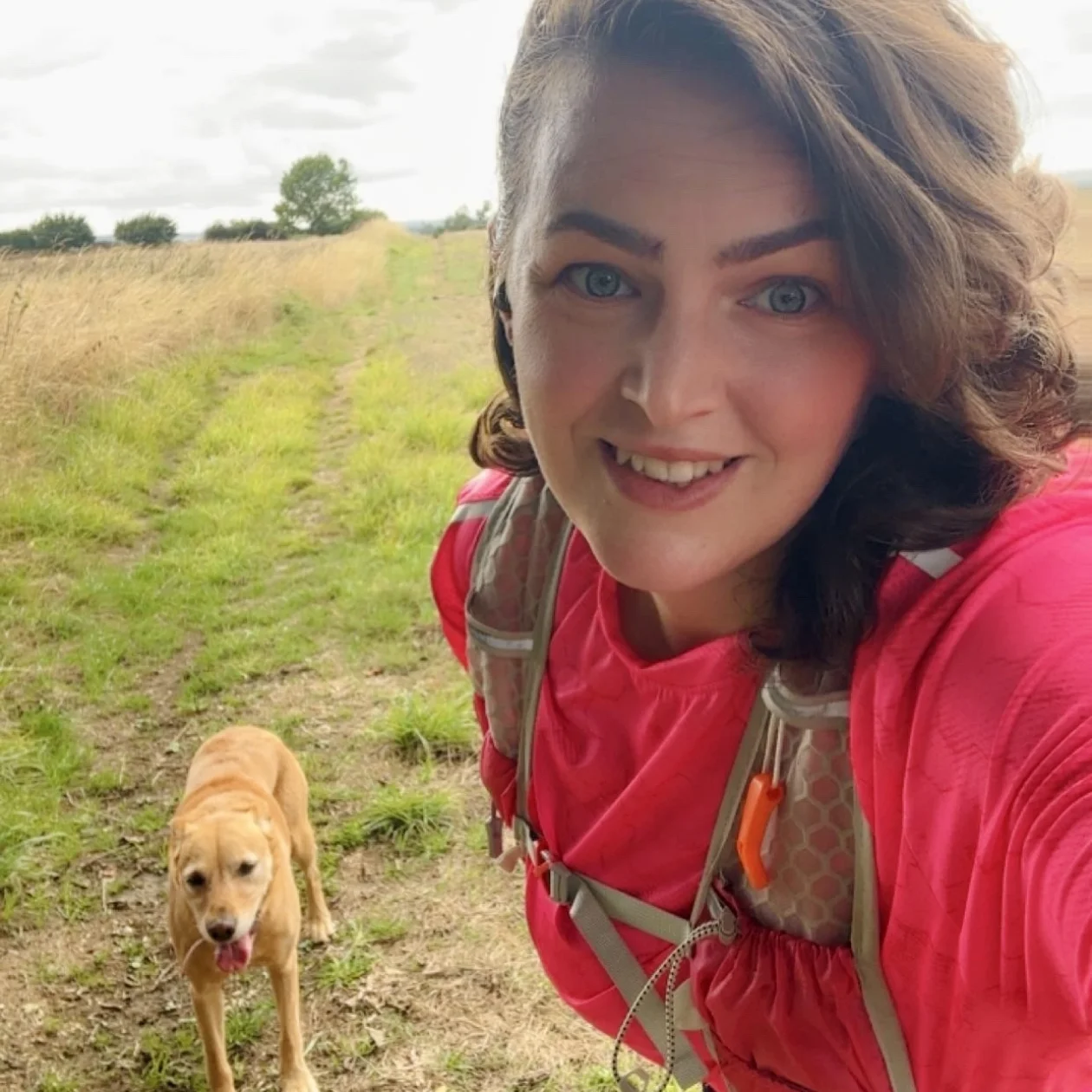 A lady walking a dog in the countryside takes a selfie
