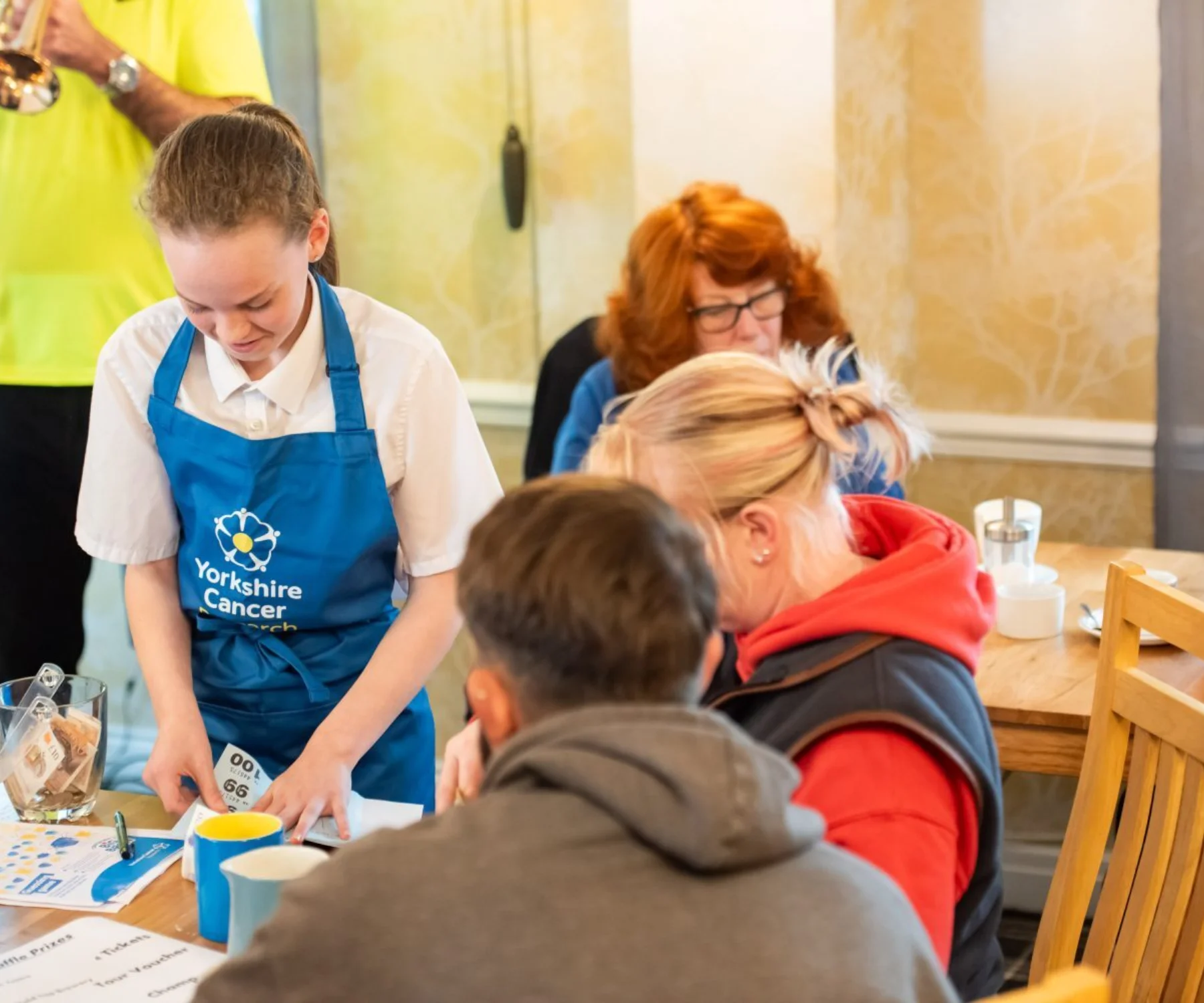 A girl pulls a strip from a raffle book to give to a lady