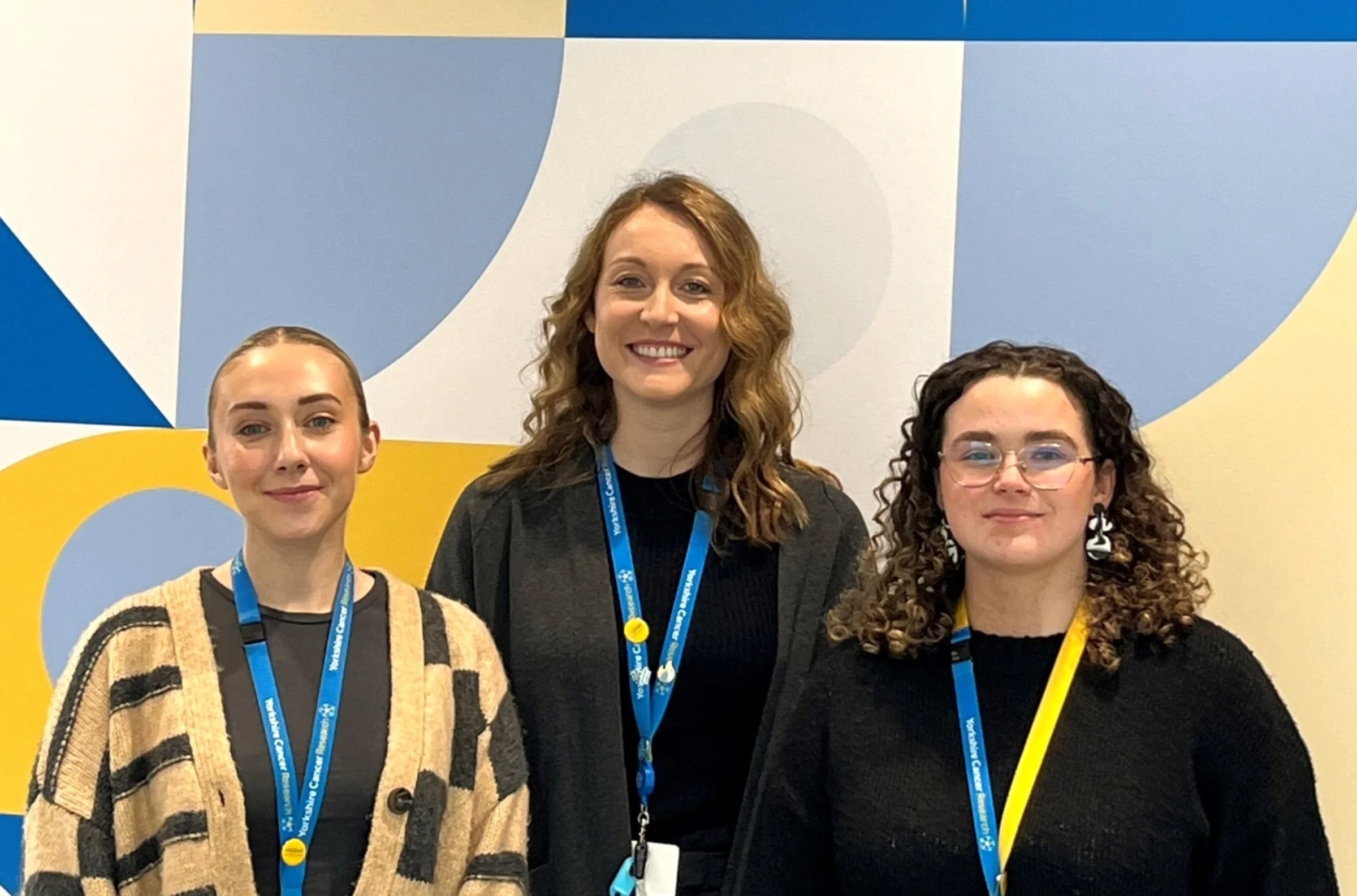 three women stand together in front of a patterned wall