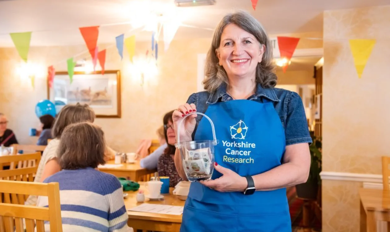 A woman stood in a cafe holding a collection pot with money in