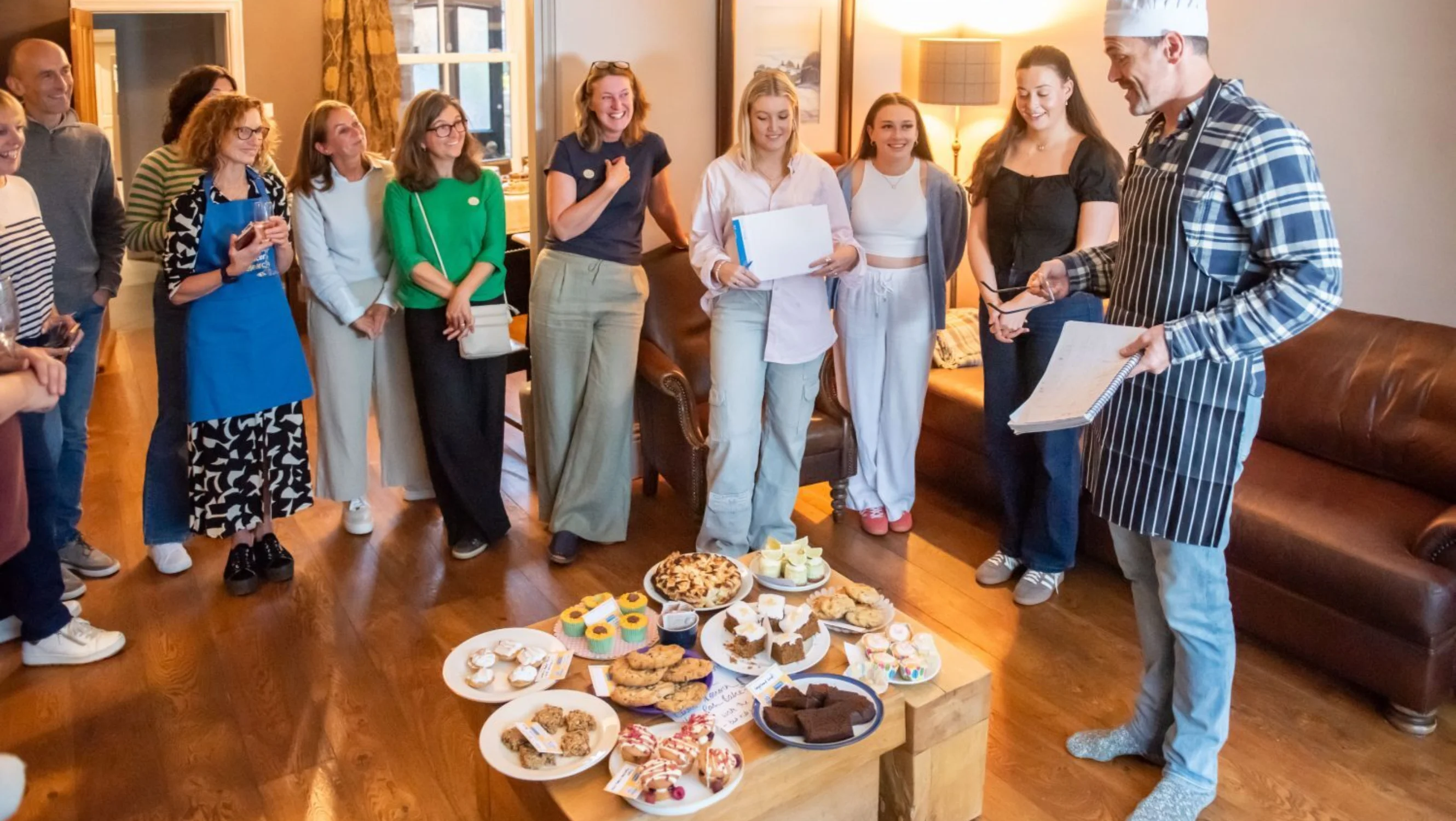 A group of people gather around a coffee table with cakes