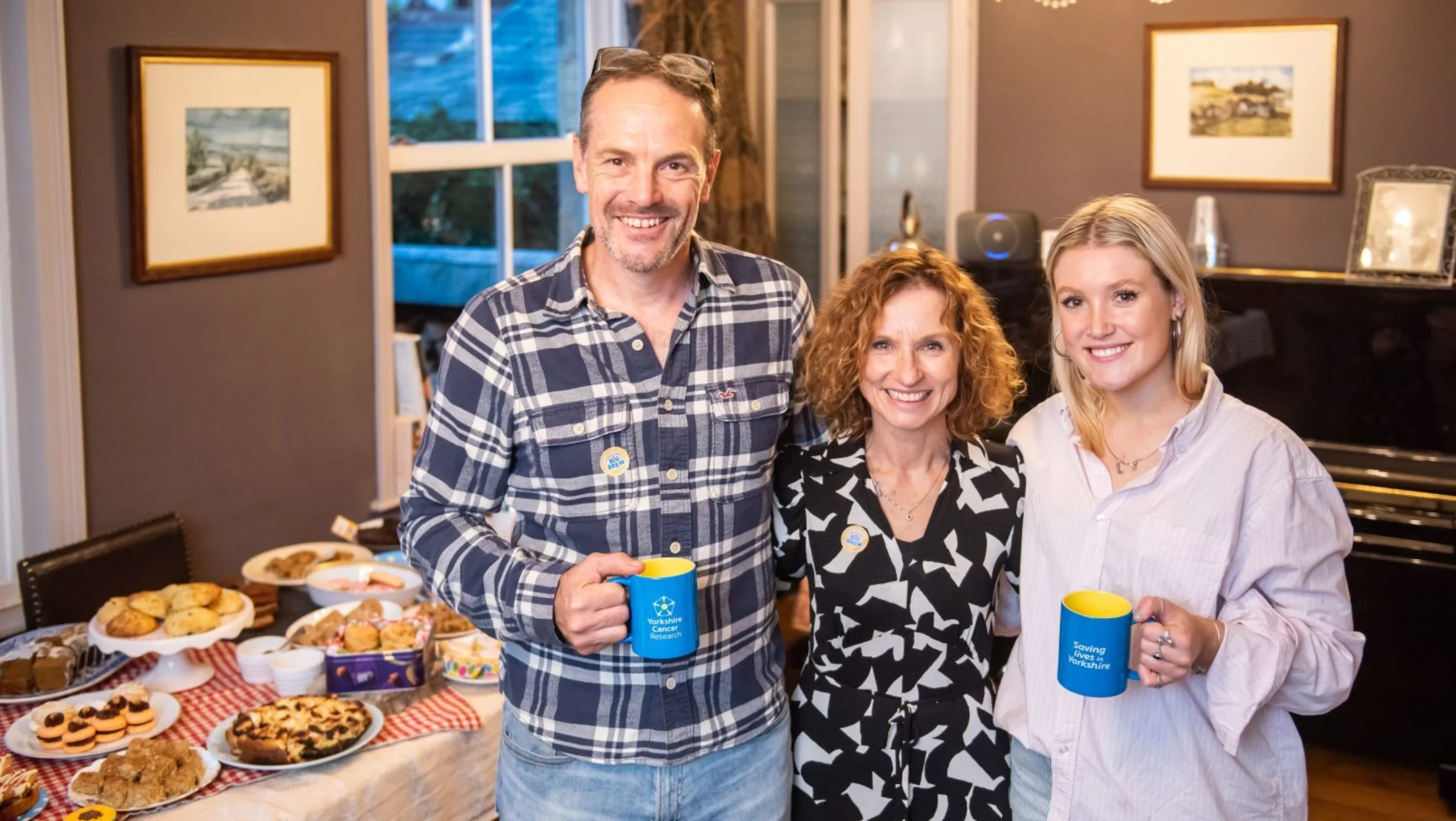A man and two women stand next to a bake sale table