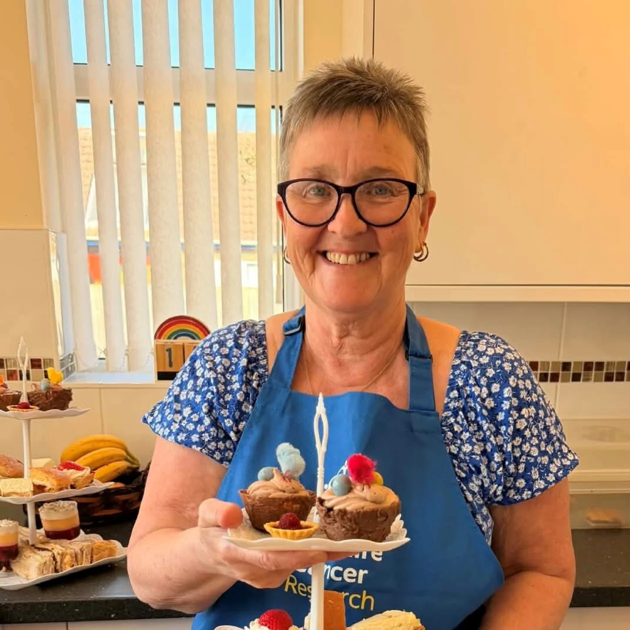A lady stands smiling, holding a cake stand