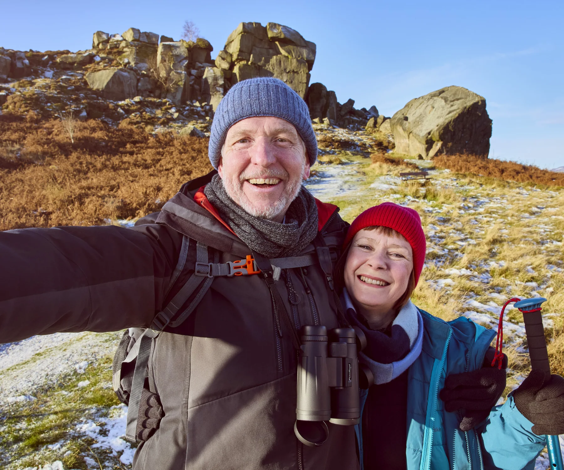 A smiling couple posing for a selfie in front of the Ilkley Moor Cow and Calf rocks.